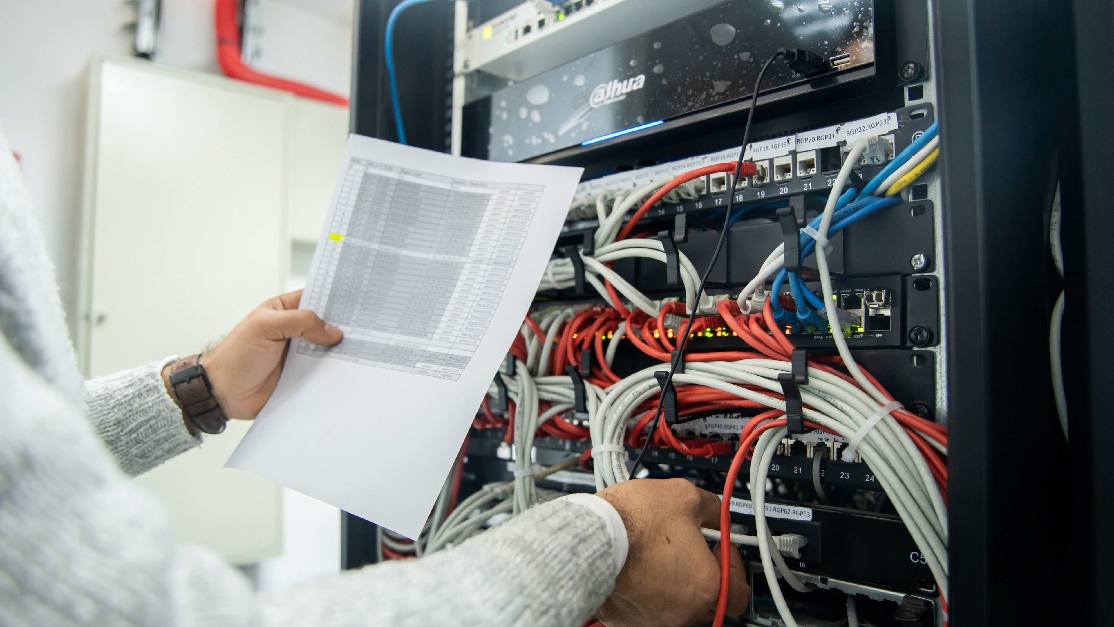 Un technicien dépanne un serveur réseau, examinant un document tout en ajustant les câbles sur un serveur monté en rack.