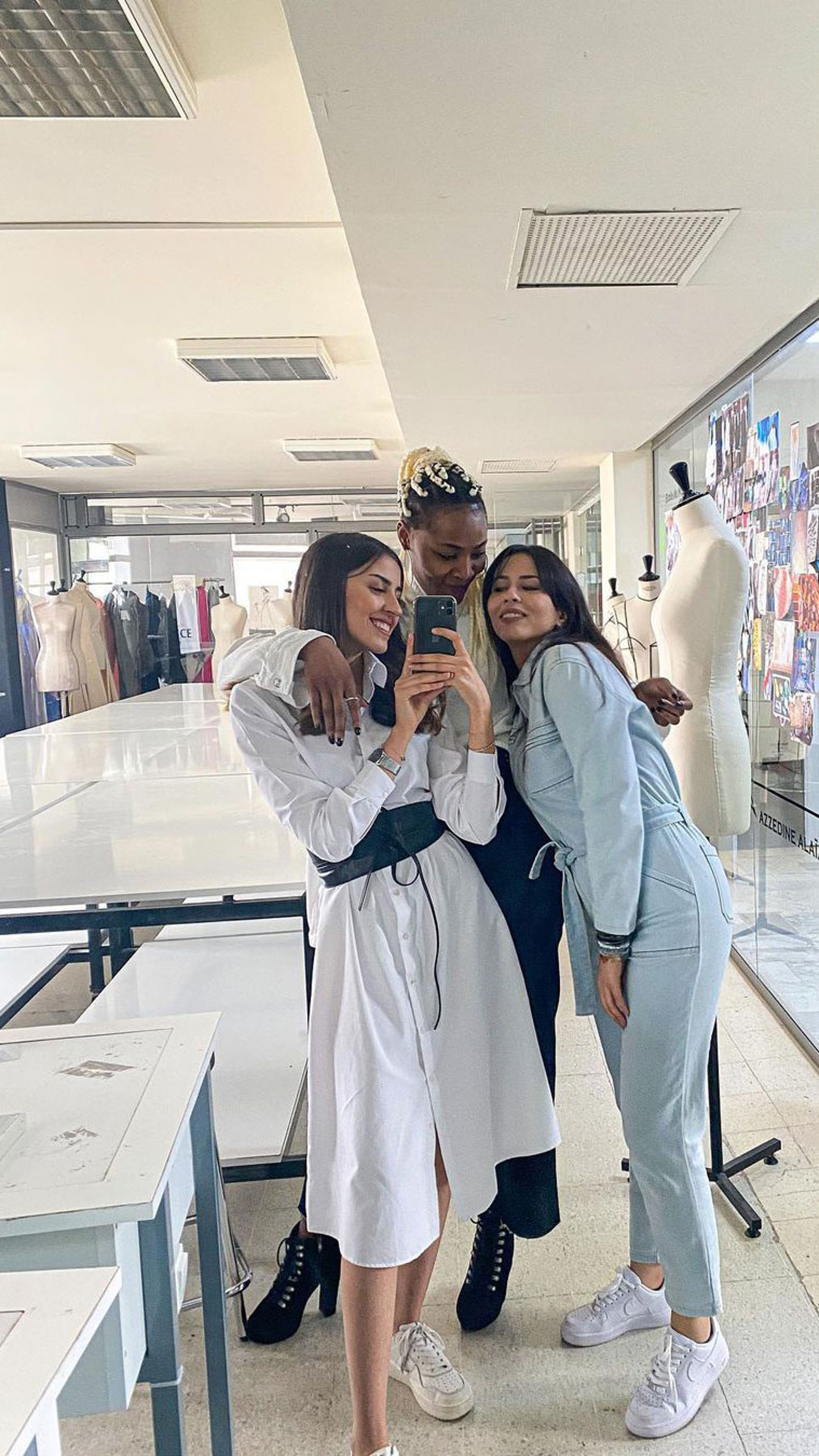 Three friends taking a selfie together in a fashion design studio, surrounded by mannequins and design sketches.