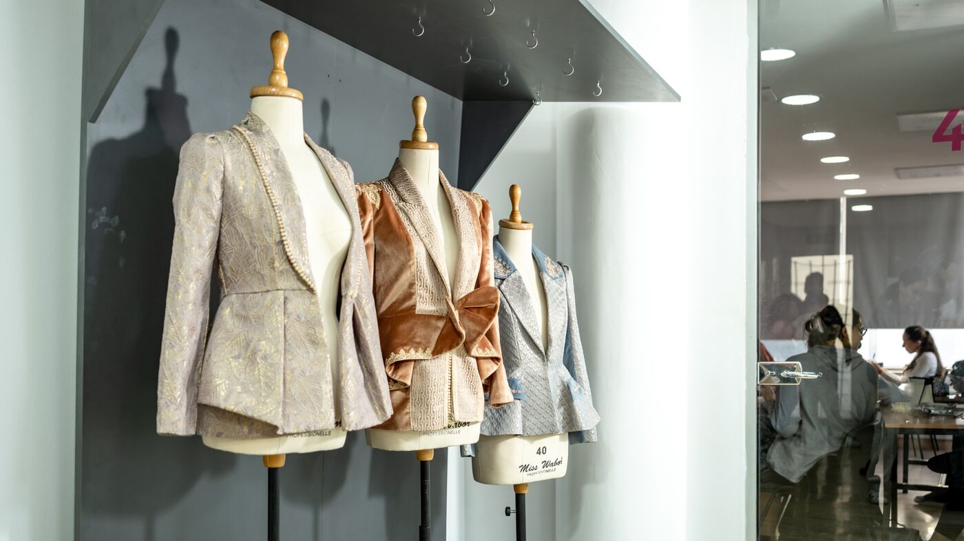 Tailored designer jackets on mannequins in a fashion design studio, with work in progress in the background.