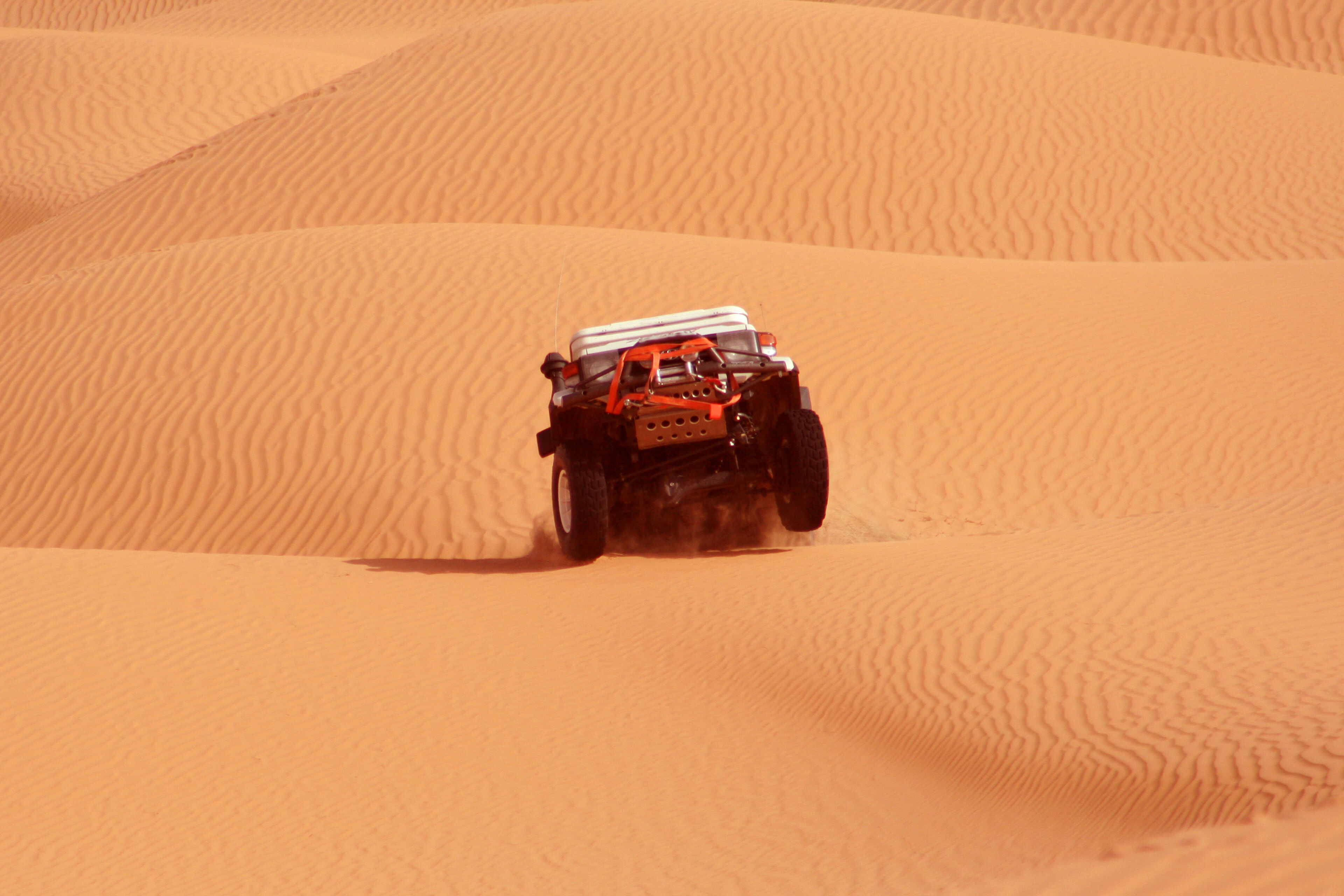 A powerful off-road vehicle conquers the desert, leaving a trail on the soft dunes under the bright sun.