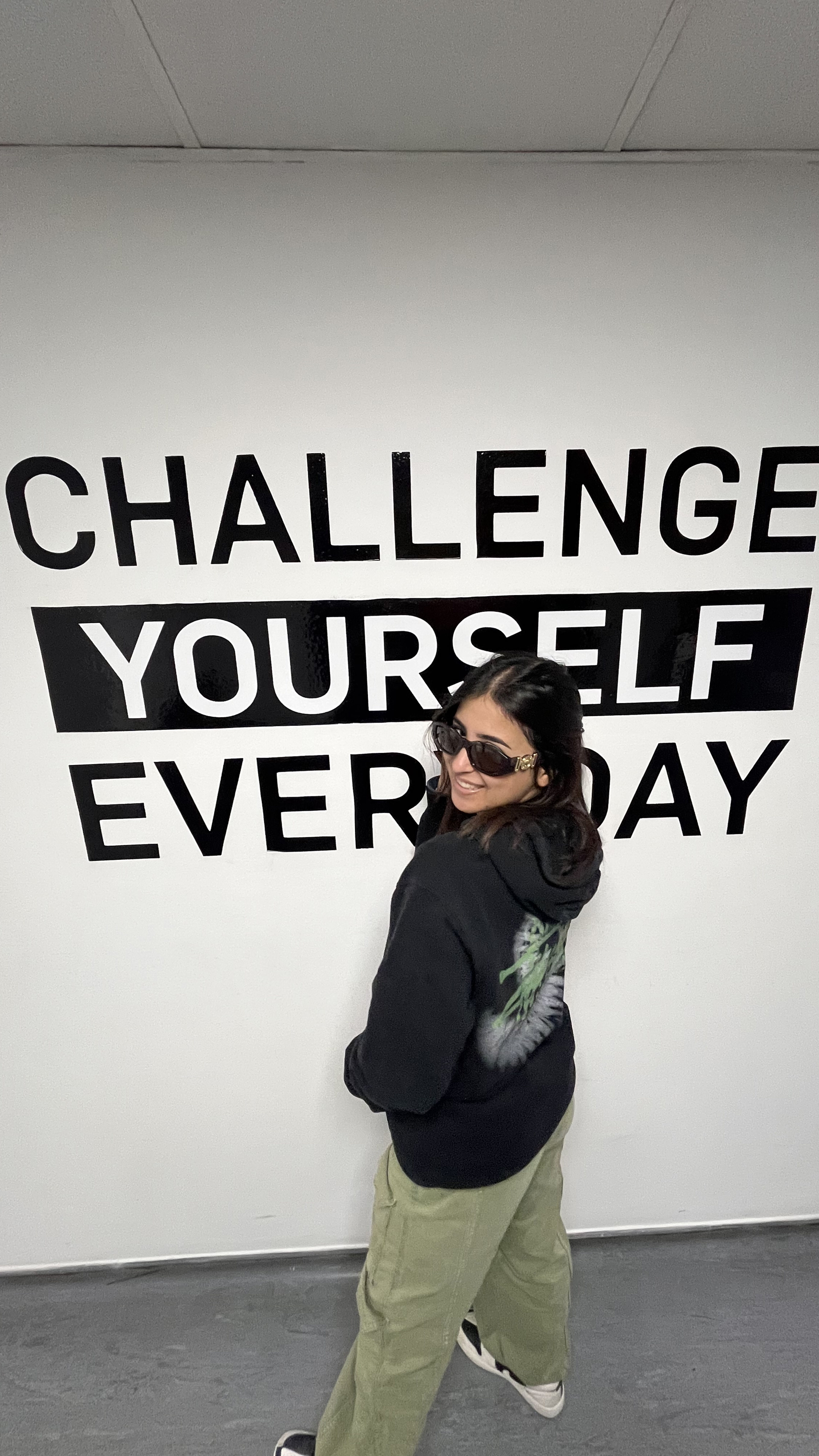 A person poses playfully in front of a wall with the motivational message "CHALLENGE YOURSELF EVERYDAY" in bold letters.