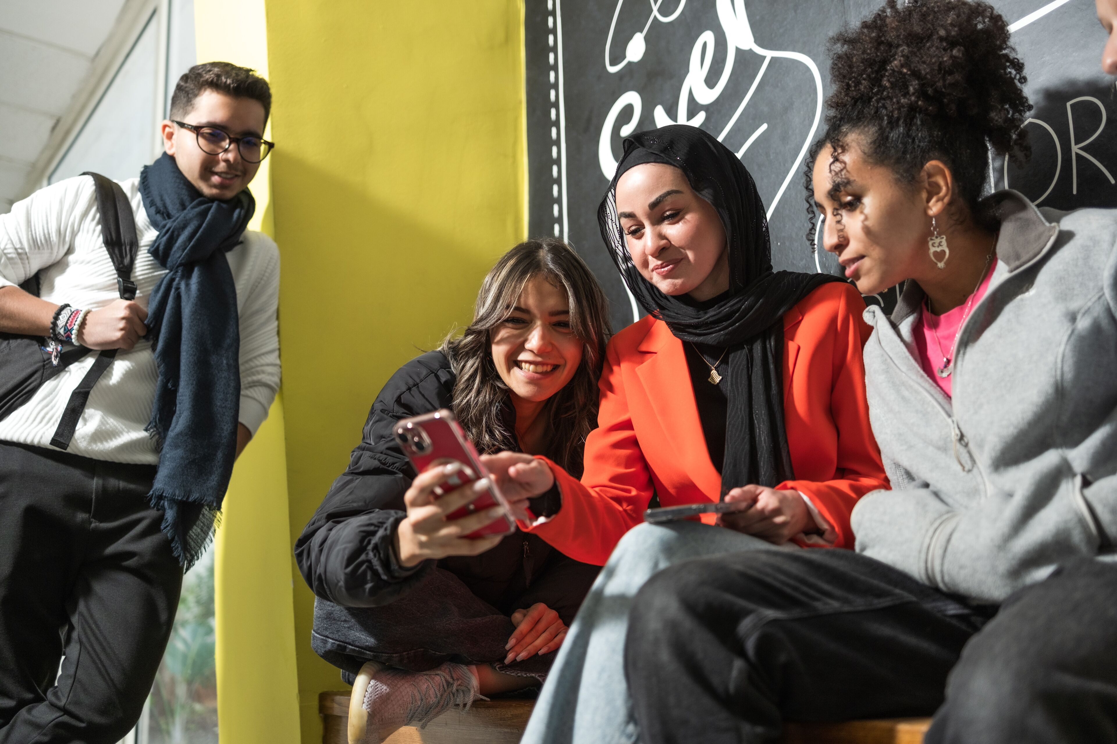 A diverse group of students sharing a joyful moment over a smartphone in a cozy campus setting