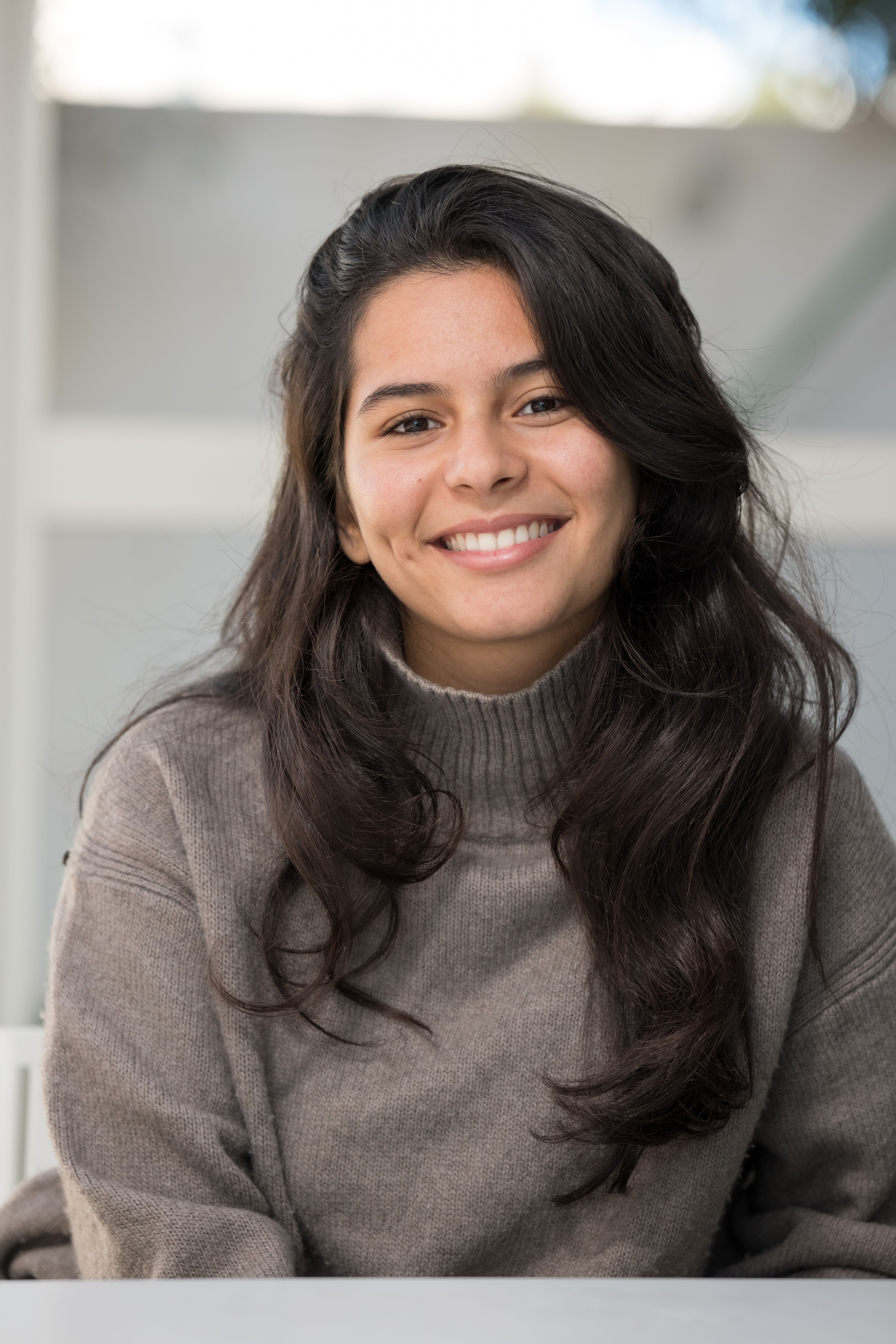 Portrait of a smiling student with long hair and a warm sweater, embodying youthful optimism and friendliness