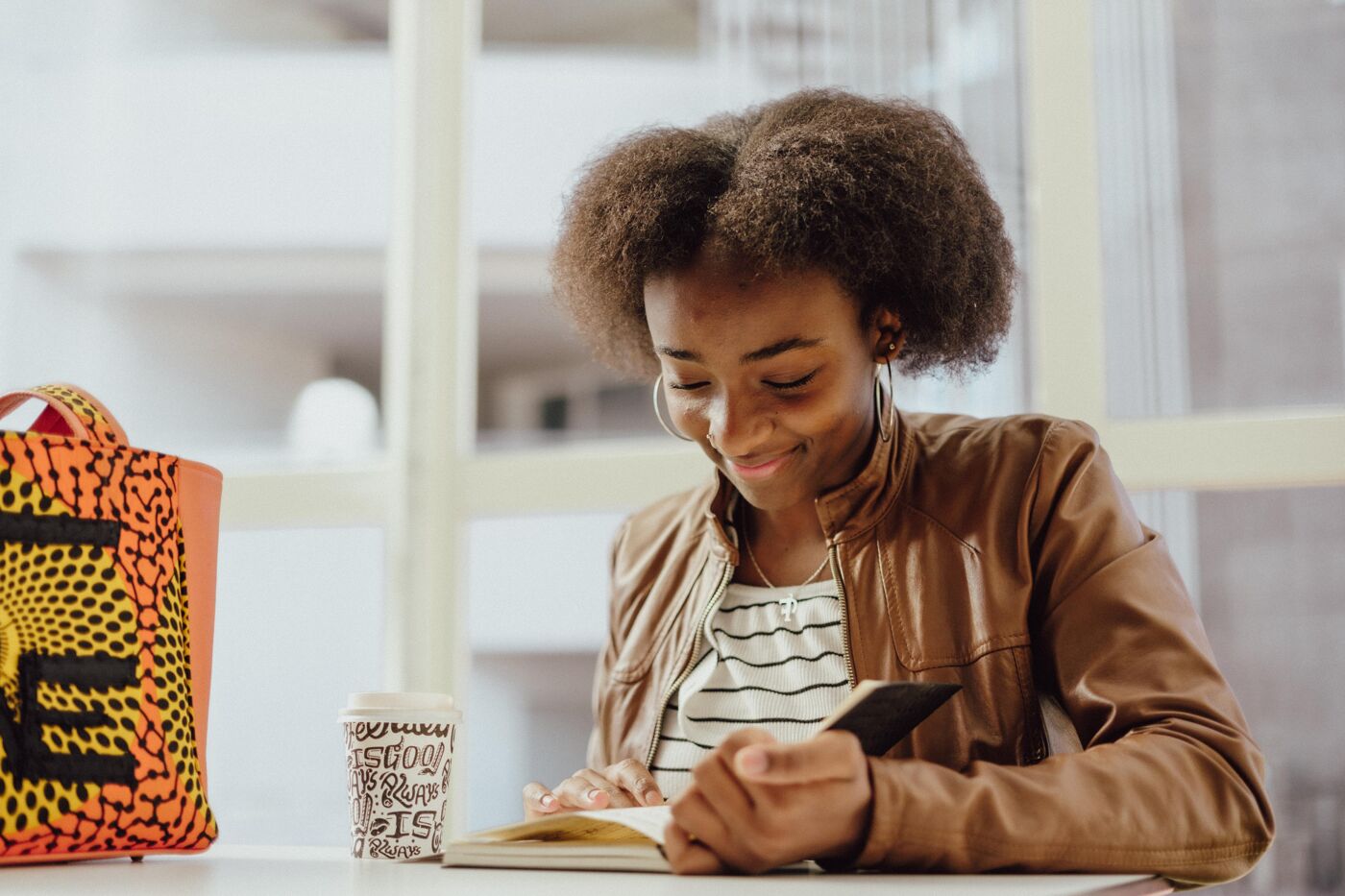 The image features a woman sitting at a table, reading a book, and holding a cup of coffee.