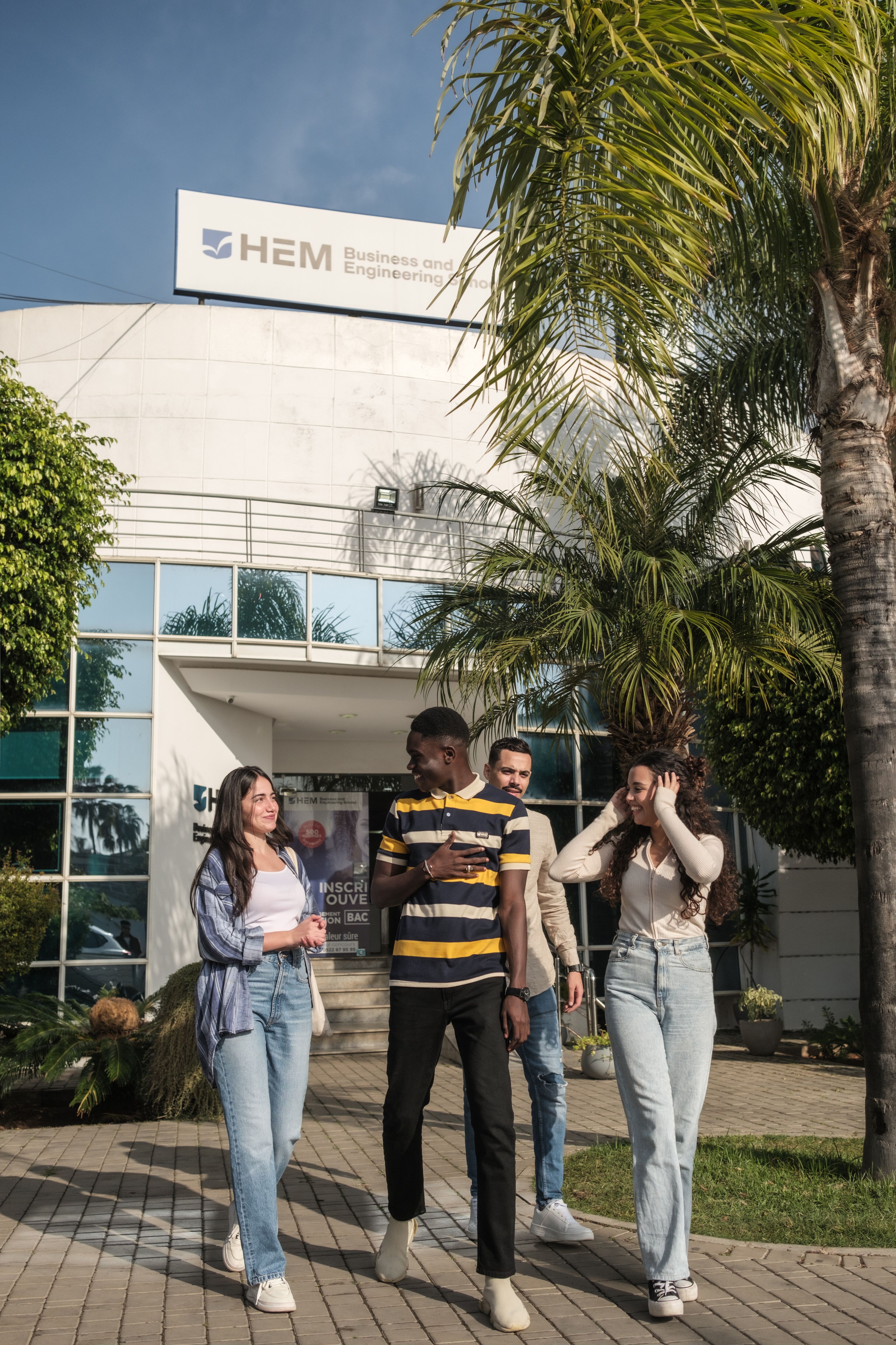 A group of young students walking and talking at the entrance of a business and engineering school campus.