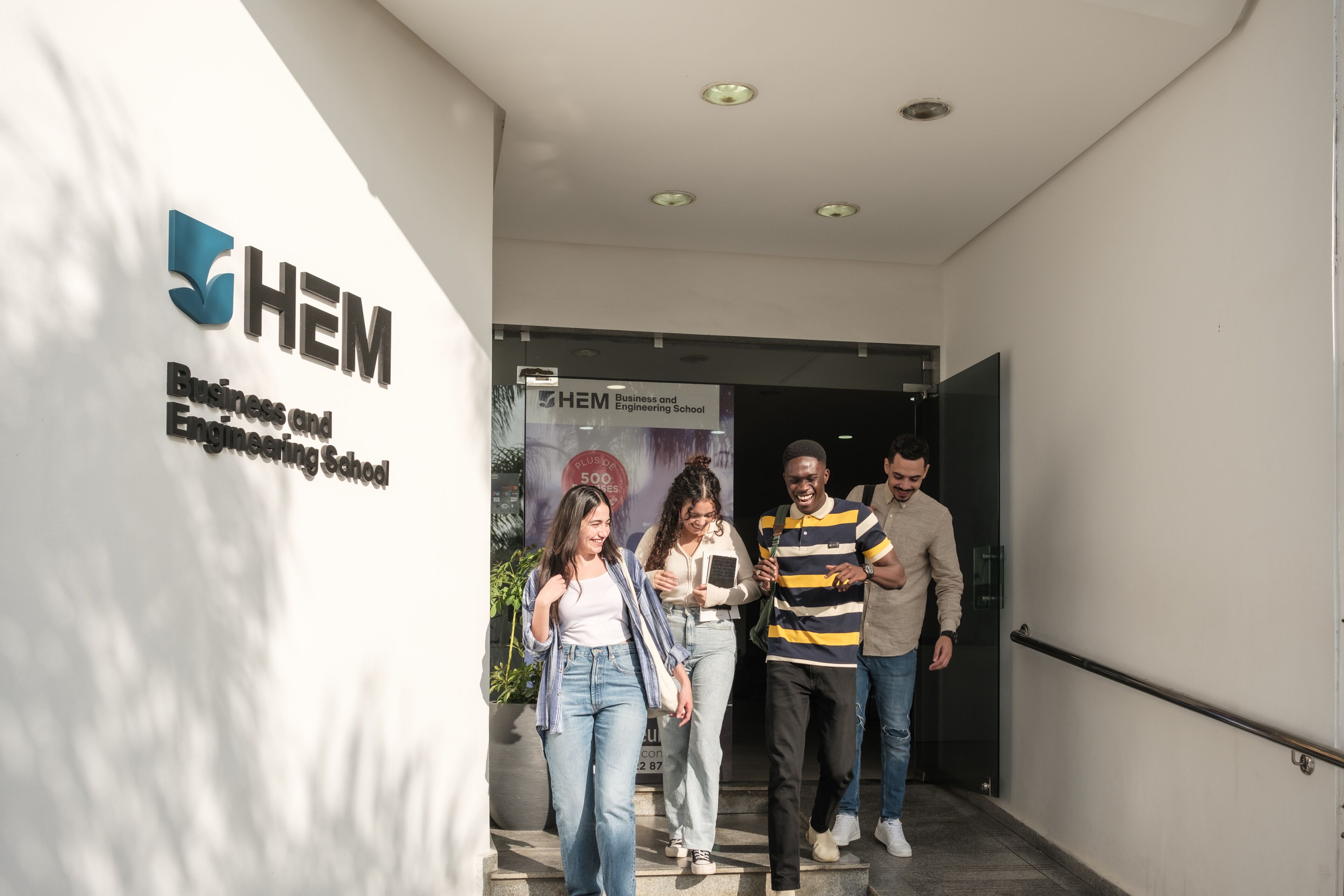 Students stepping out of a business and engineering school, engaged in cheerful conversation.