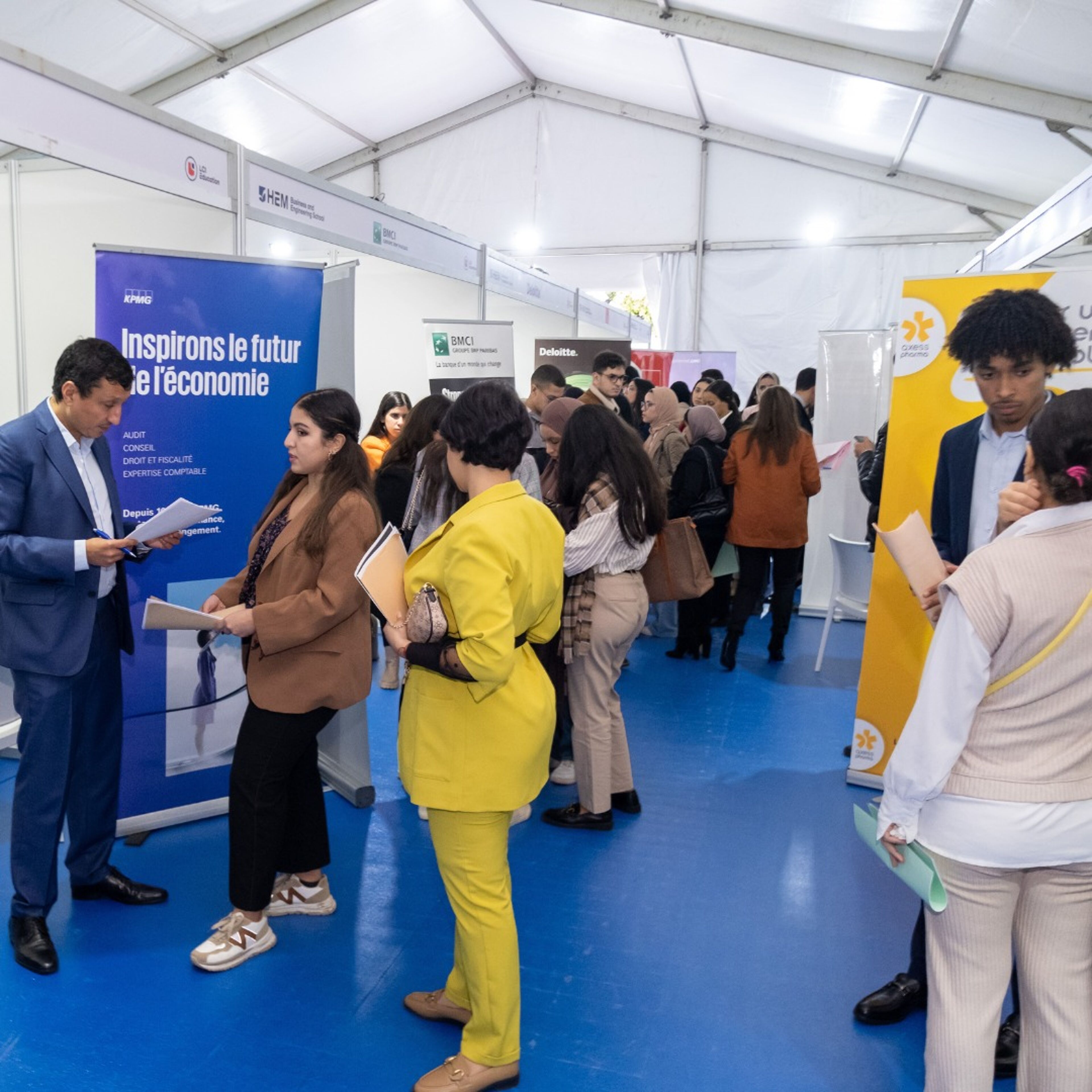 Professionals and students interacting at various booths during a career fair in a tented space.