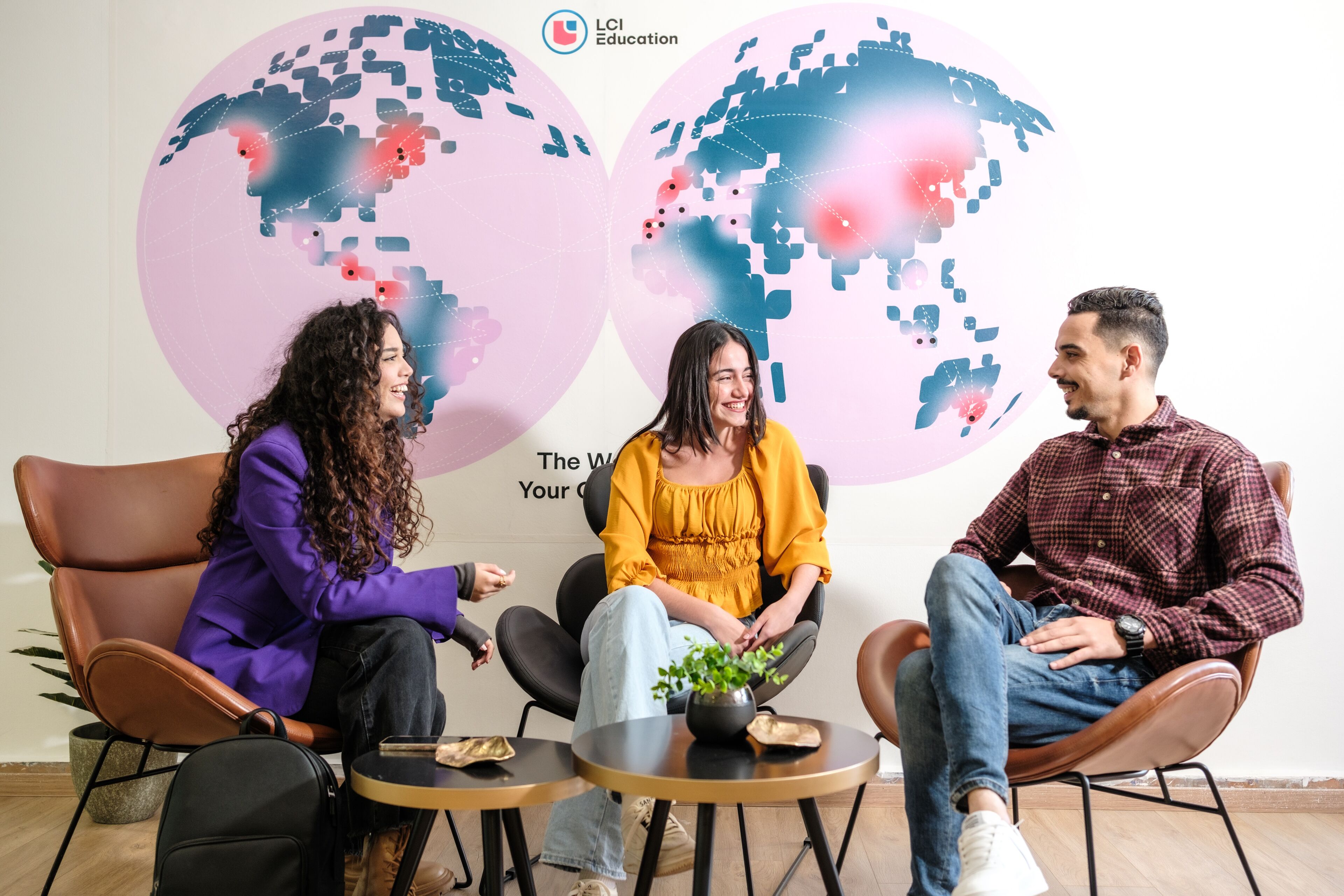 Three people casually conversing in a vibrant setting with world map graphics in the background, symbolizing international education.