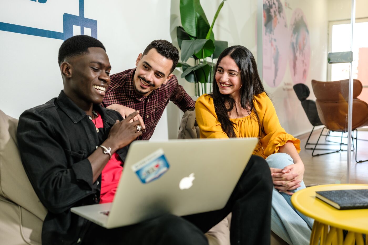 A group of three diverse professionals engaging with a laptop in a casual office environment, reflecting teamwork and collaboration.