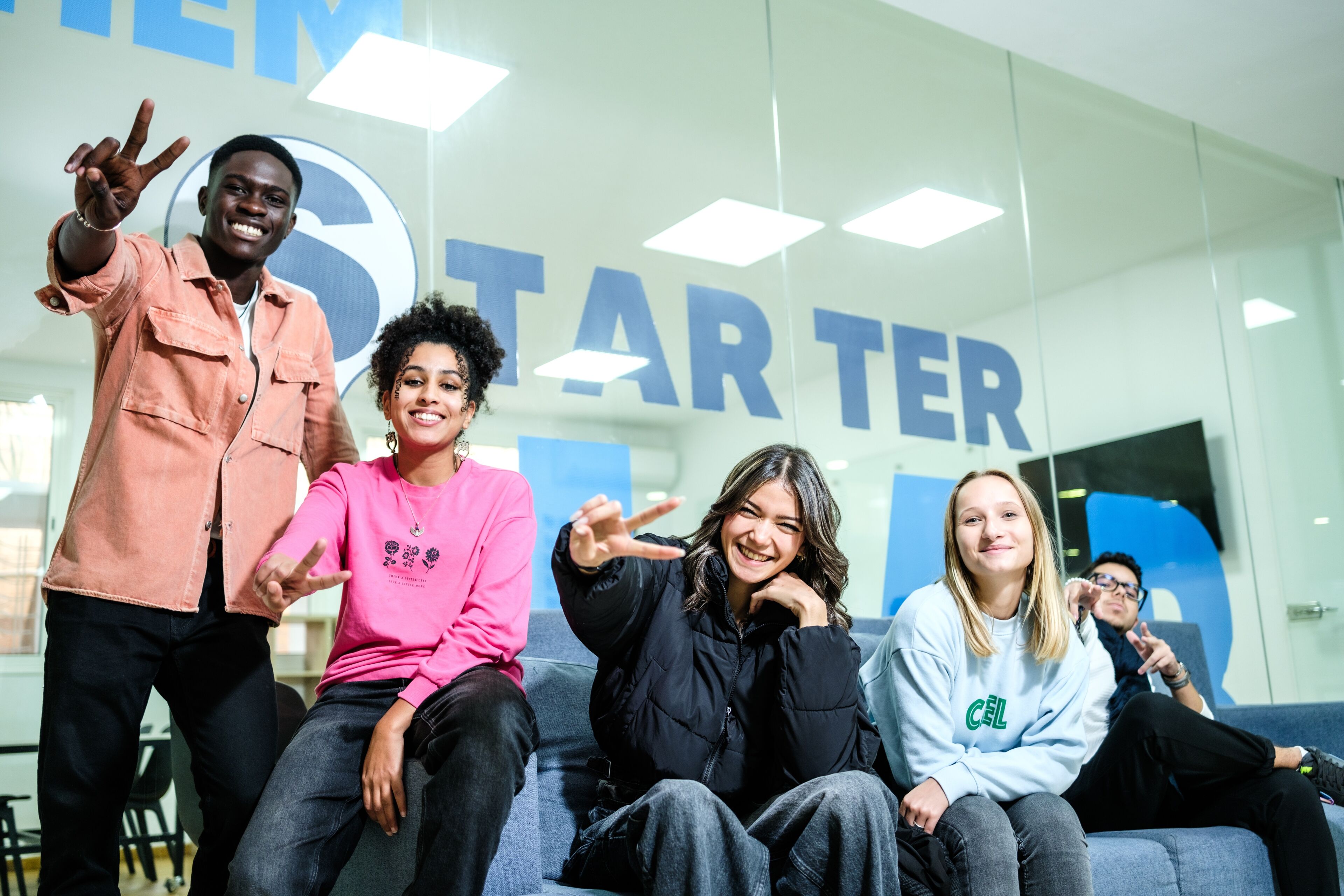 A diverse group of young adults posing with playful hand gestures in a modern startup office environment.
