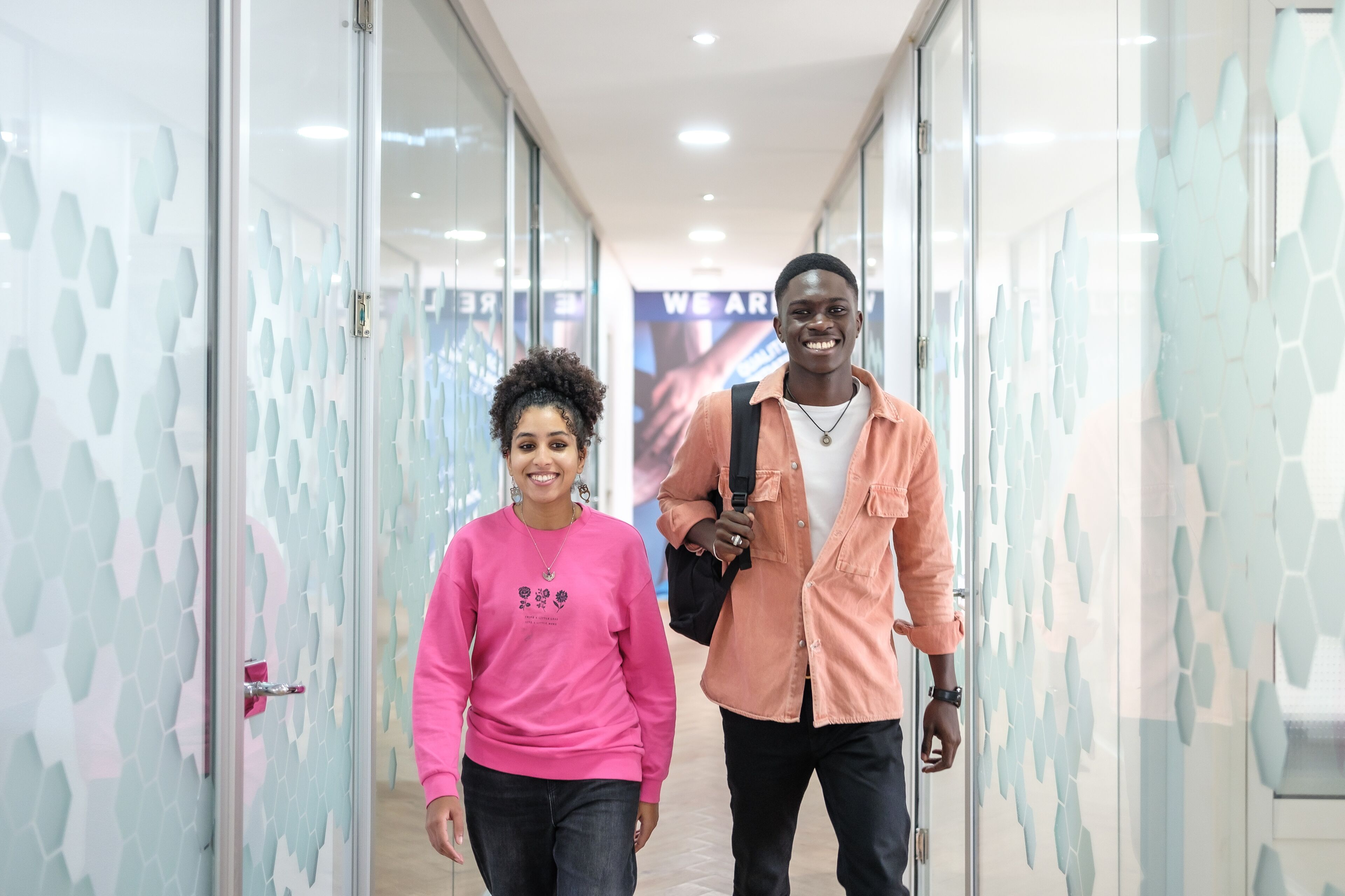 Two cheerful students walking through the corridor of a university, exuding positivity and confidence.