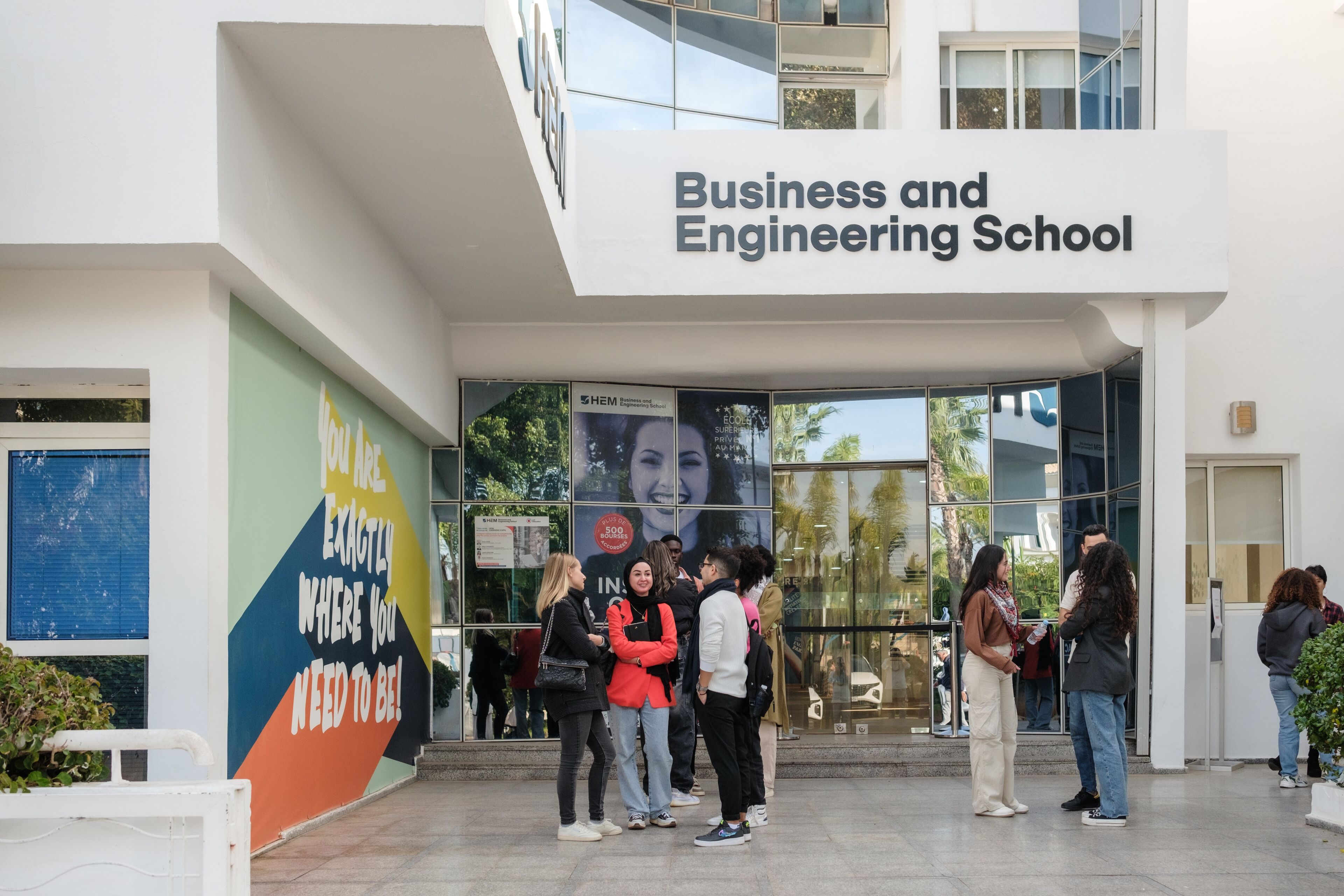Students gather at the entrance of the Business and Engineering School, surrounded by modern architecture and a motivational banner.