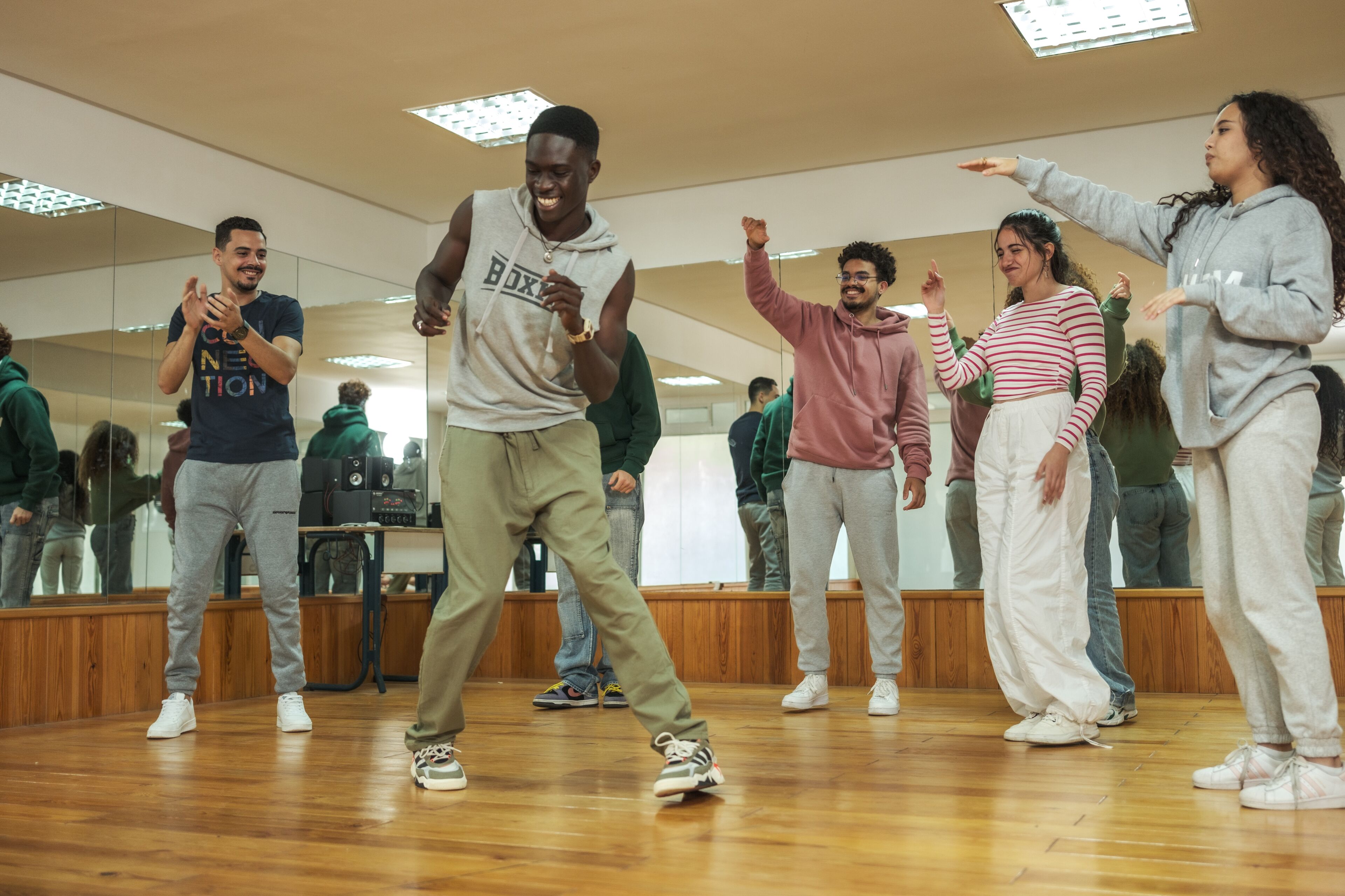 A group of people laughing and dancing in a dance studio, with one person in the center enjoying the moment, reflecting a lively dance session.