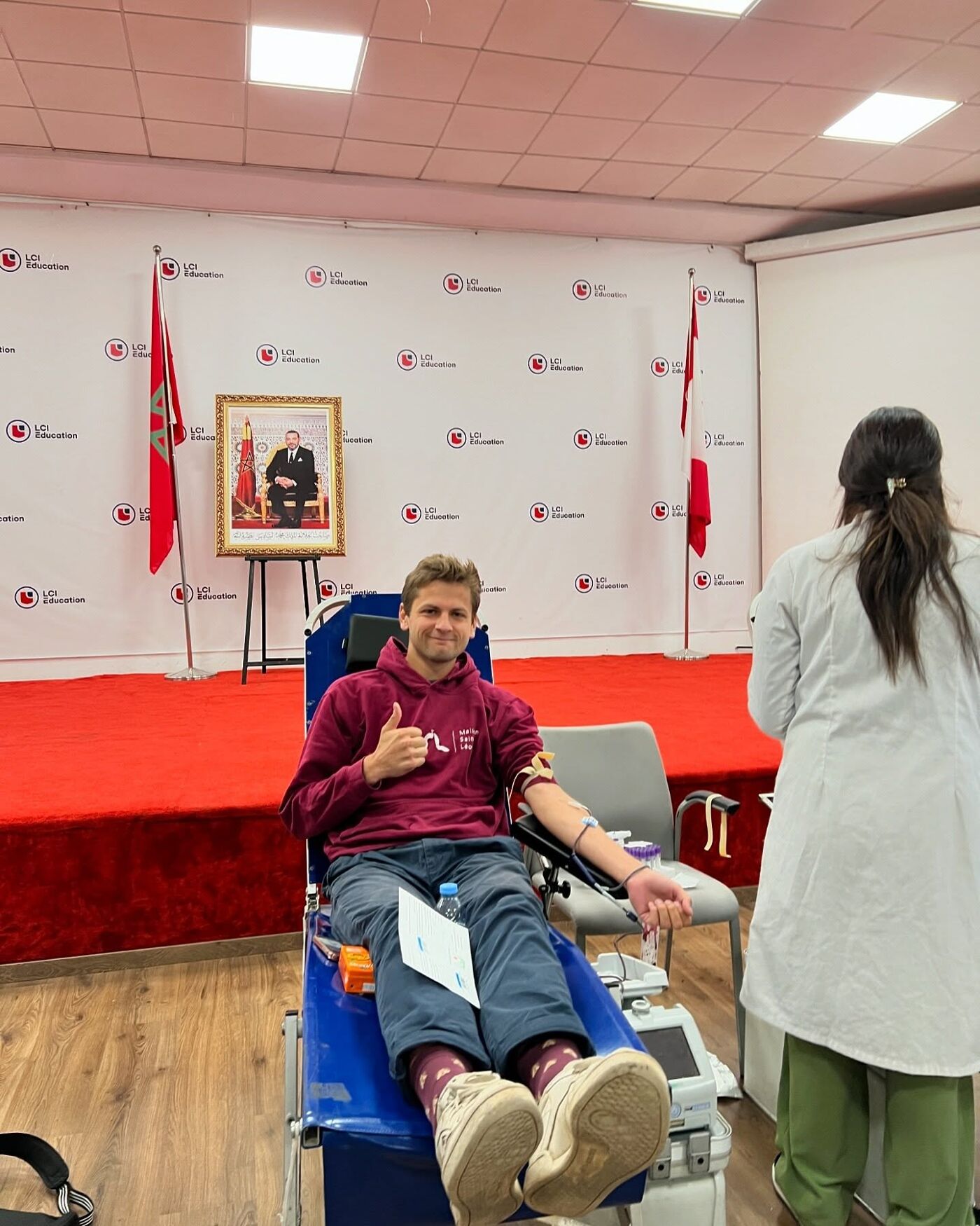 In the image, a man is sitting in a wheelchair, receiving a blood transfusion from a nurse.