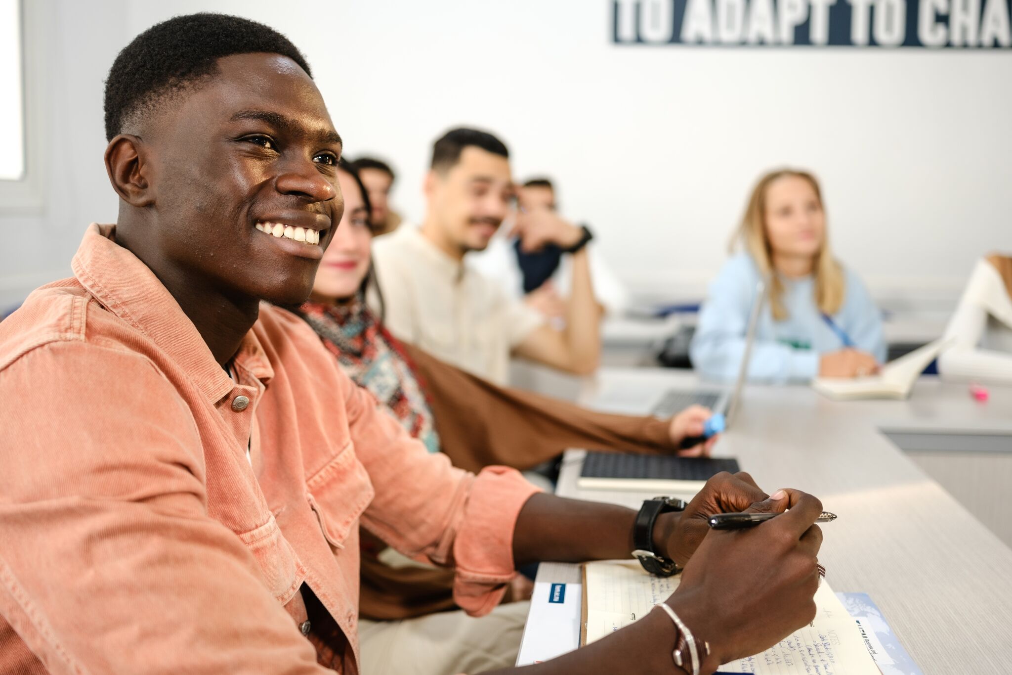 A student with a bright smile engages in classwork, surrounded by peers in a collaborative learning environment.