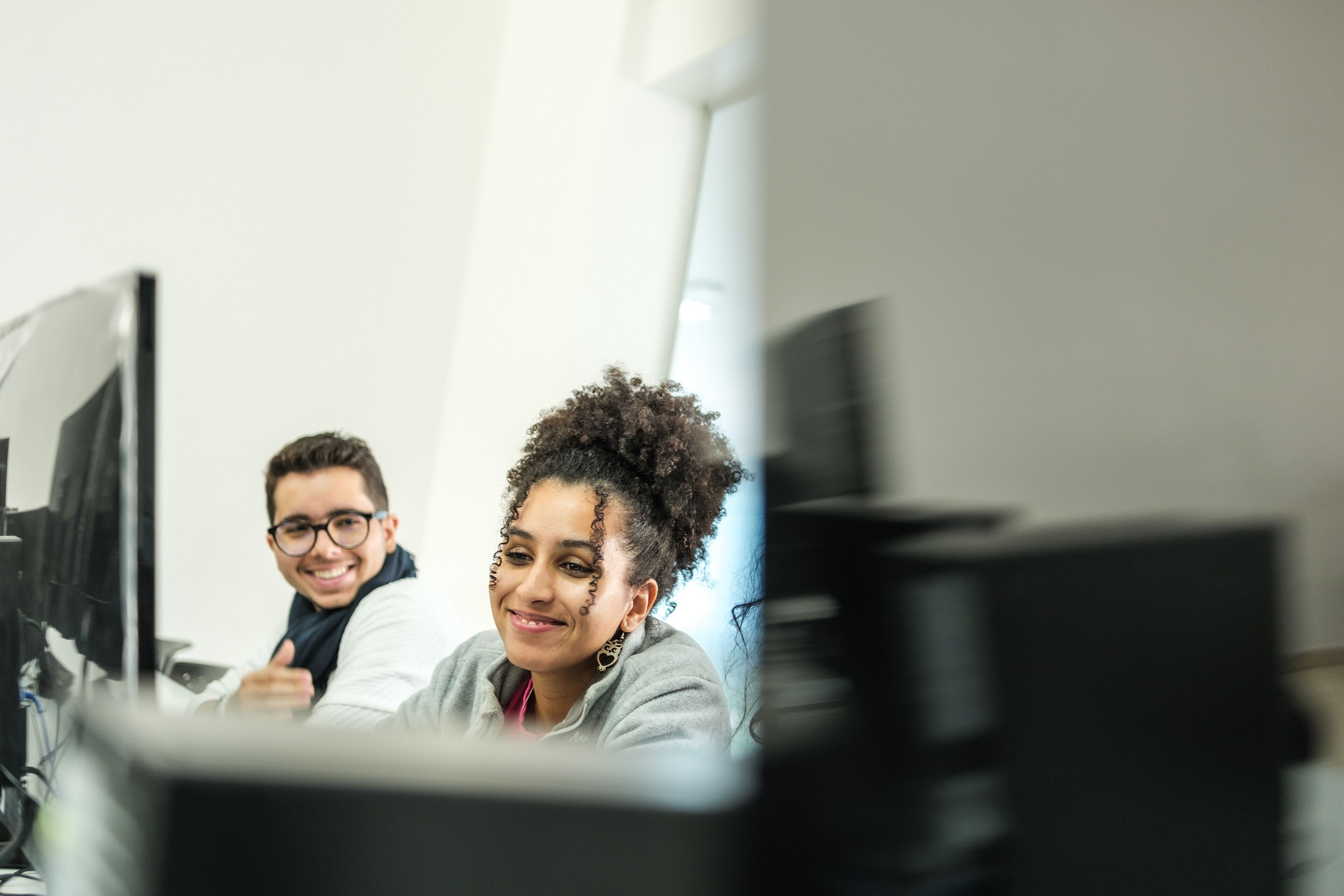 Des étudiants souriants travaillant sur des ordinateurs dans une salle de classe bien éclairée, démontrant l'intégration de la technologie dans l'éducation.