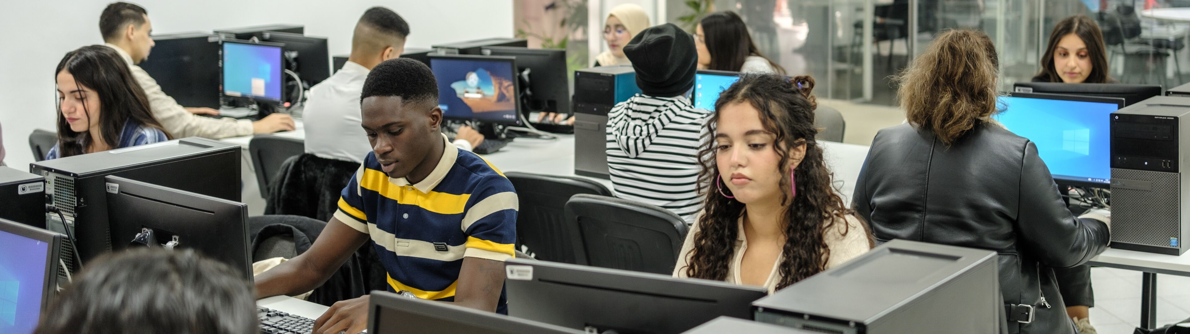 Des étudiants travaillant avec application dans une salle informatique équipée de PC de bureau.