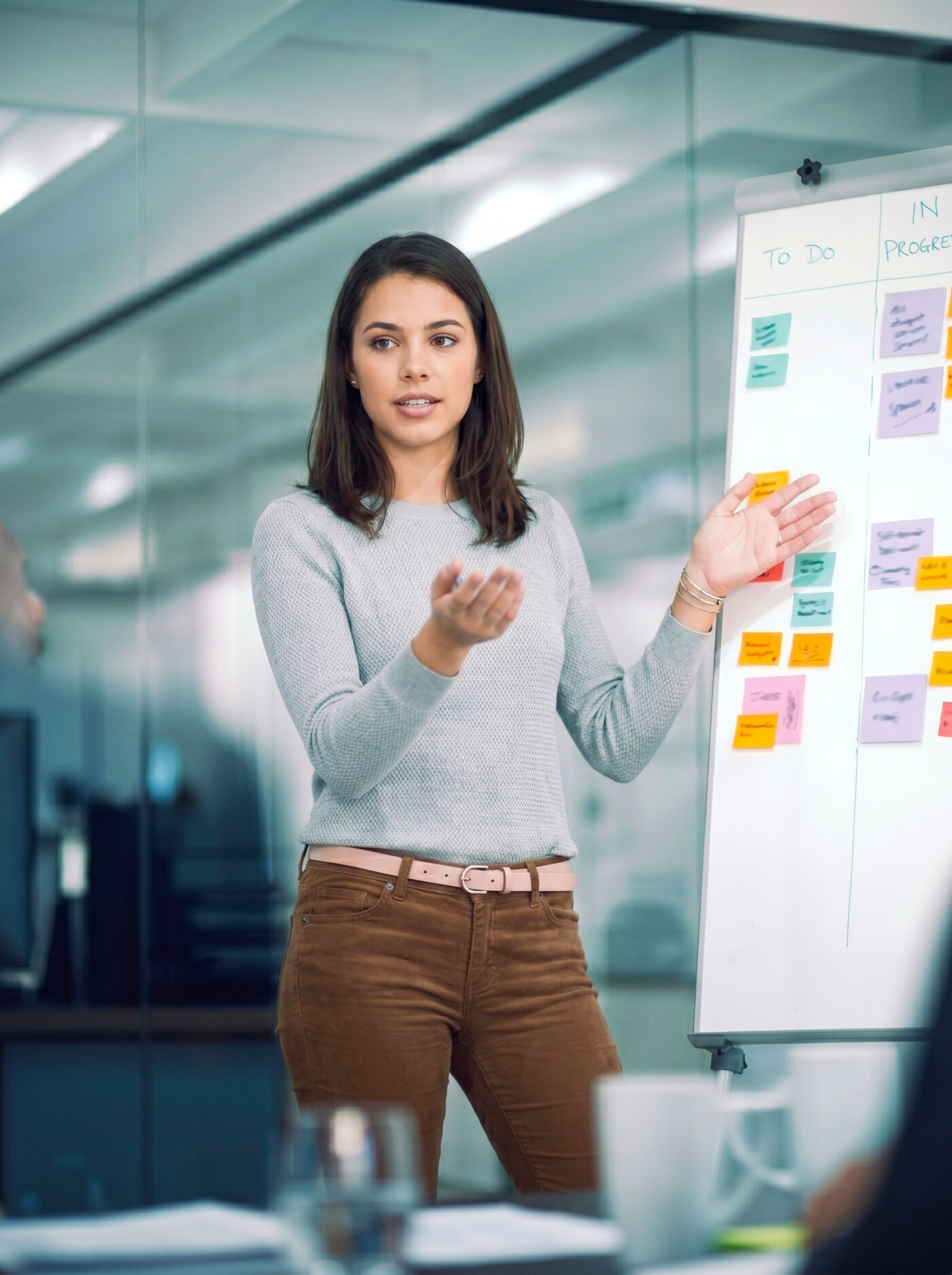 A young woman presents an action plan during a business meeting, using a whiteboard with sticky notes to visualize tasks and progress.