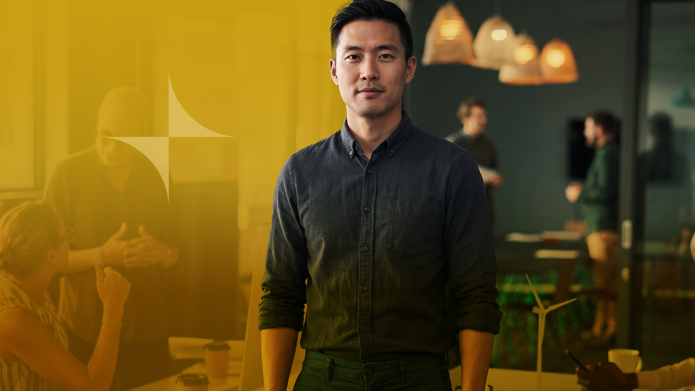 A confident Asian man stands in front of a diverse team working in a modern office setting, with a yellow logo overlaid.