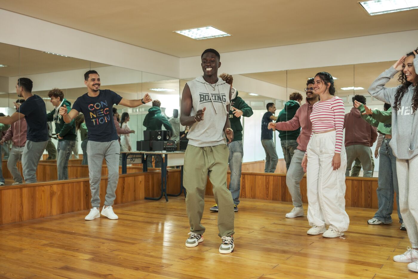 A diverse group of people joyfully participate in a dance class, following the instructor's moves in a mirror-walled studio.