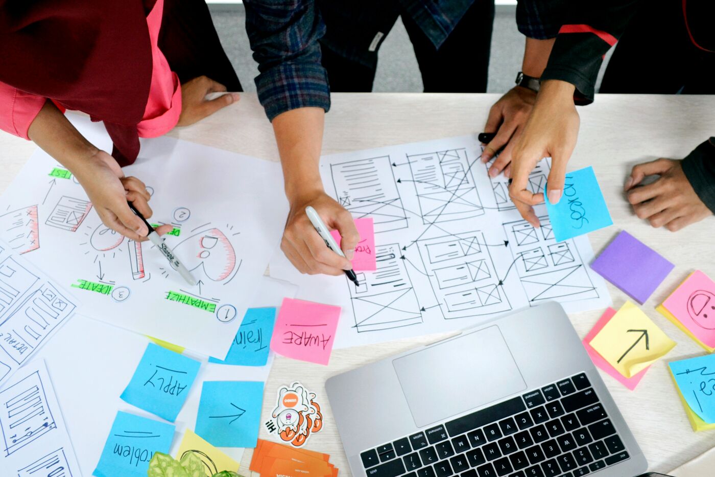 A team of designers collaborates on a project, using sticky notes and sketches to plan a website or app.