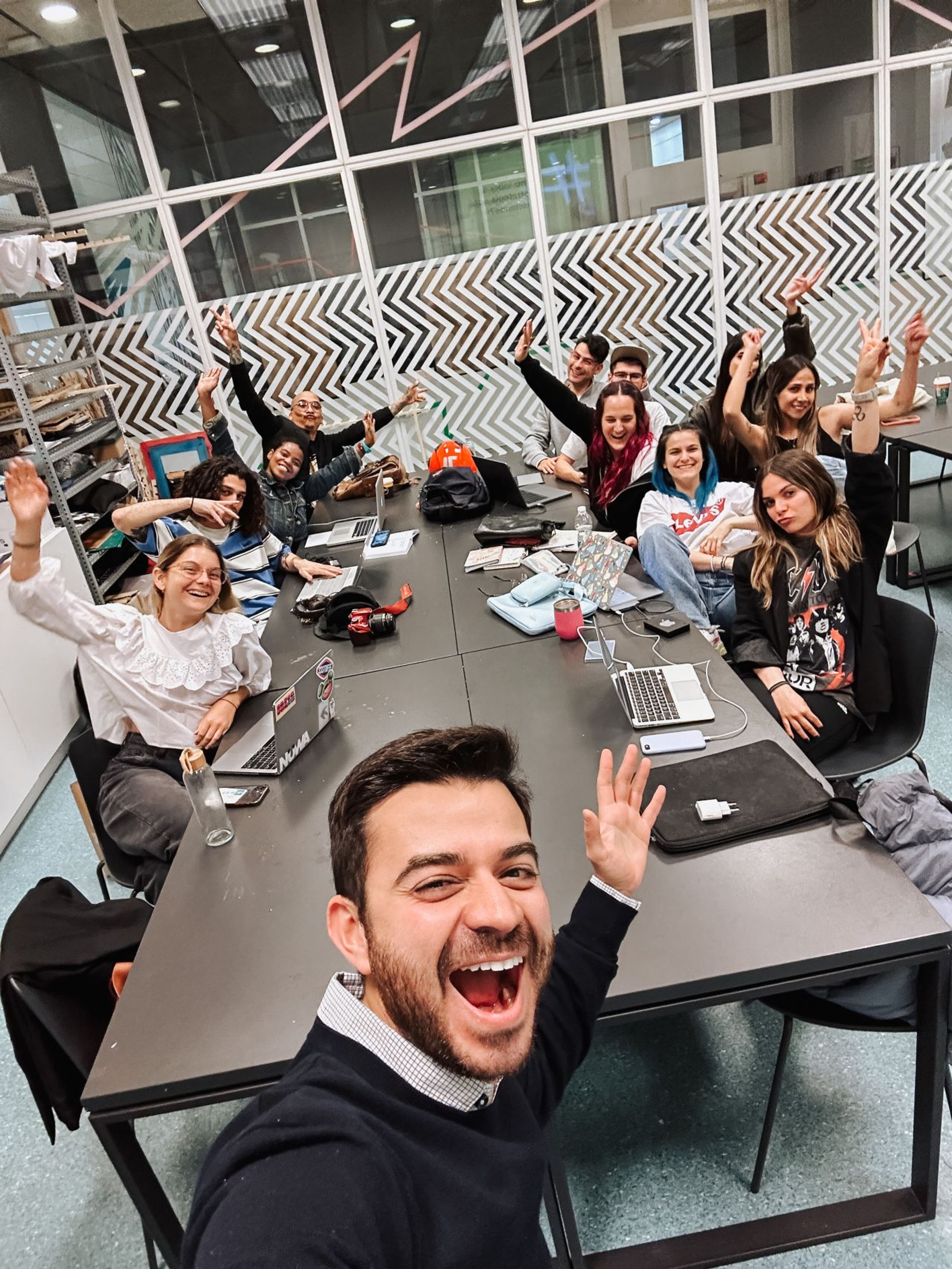 A spirited team expresses joy in a collaborative workspace, laptops open and hands raised in a cheerful, united gesture.