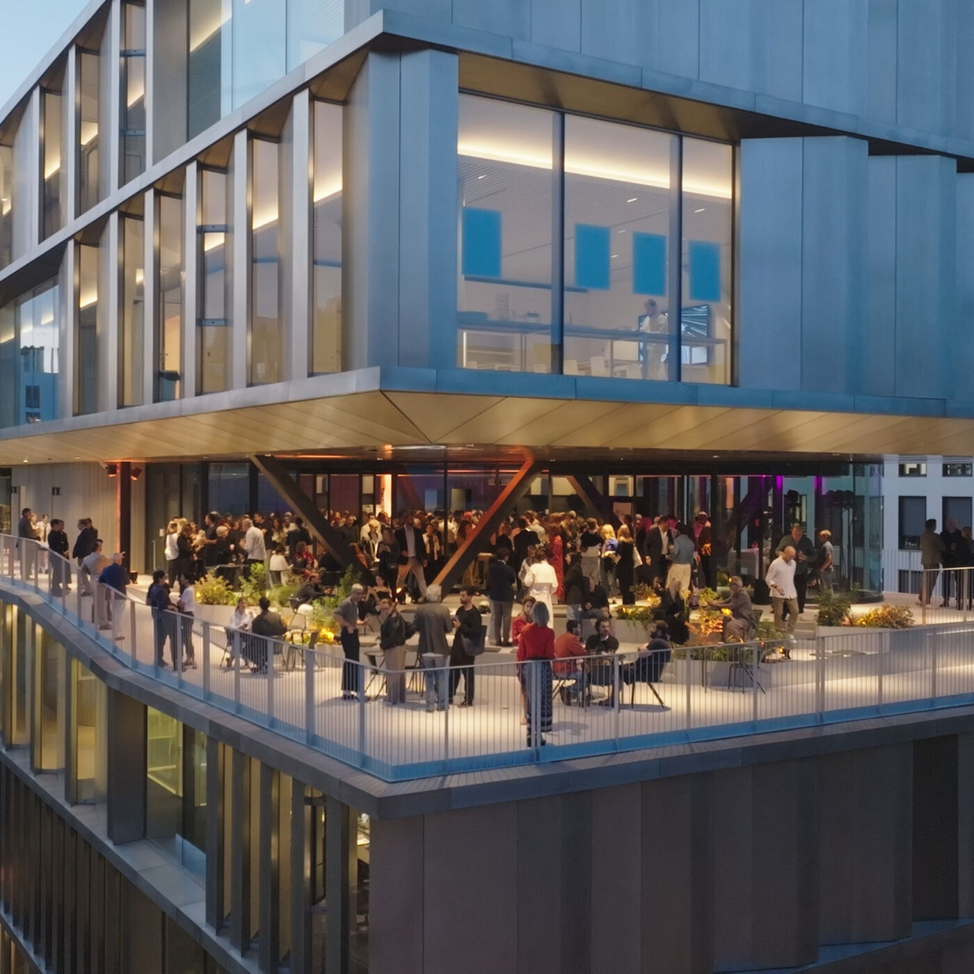 The image shows a rooftop gathering with many people on a modern building. The event appears to be a social gathering or party, with attendees enjoying the outdoor space and city views.