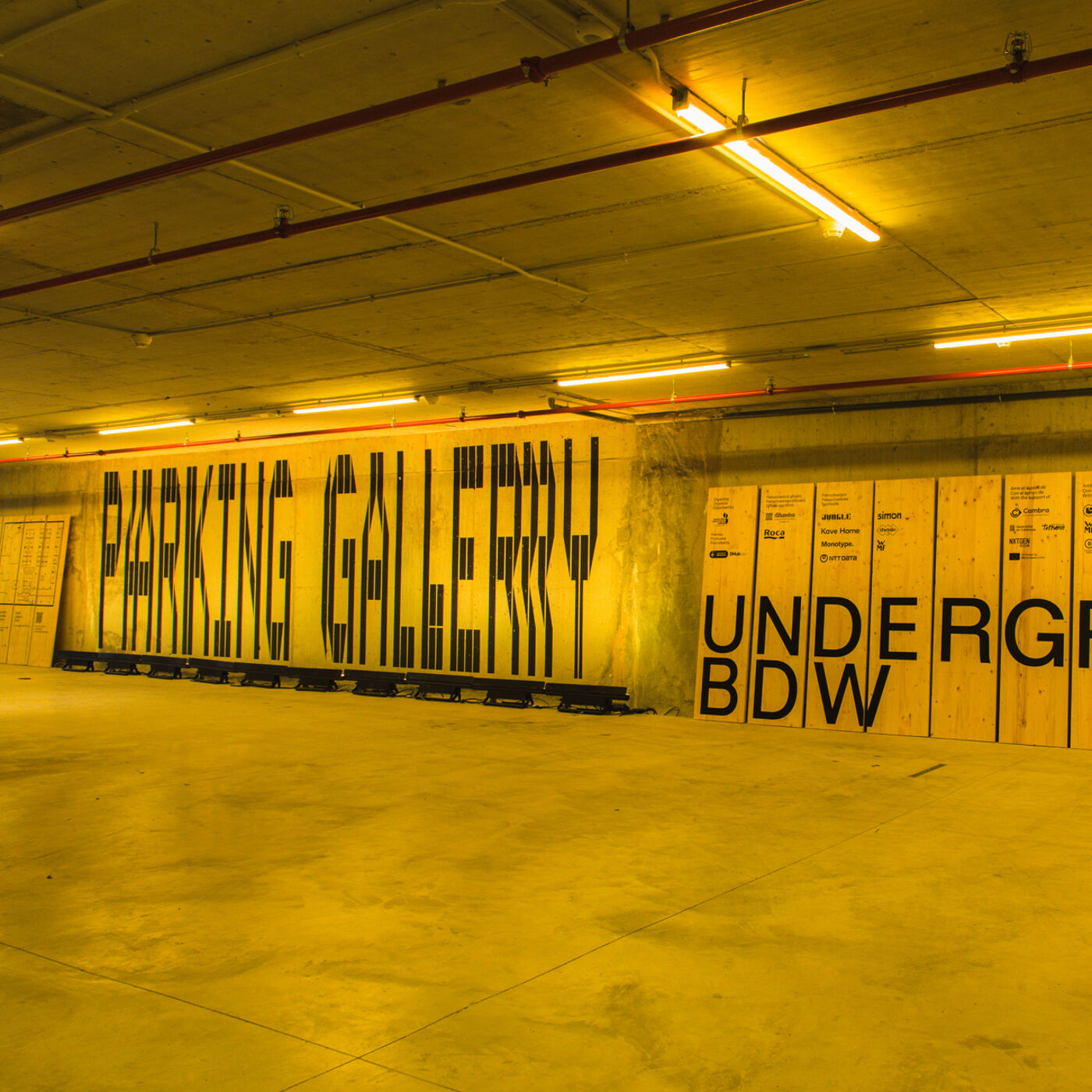 The image shows a parking gallery with the words "PARKING GALLERY" written in large black letters on a concrete wall. Next to it, the word "UNDERGROUND" is written on wooden boards. The scene is illuminated with yellow lighting.