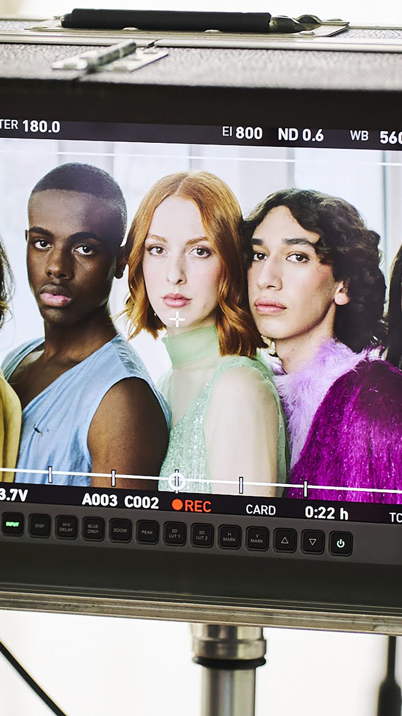 A close-up shot of a monitor displaying a behind-the-scenes image of four young actors, two men and two women, during a film shoot.