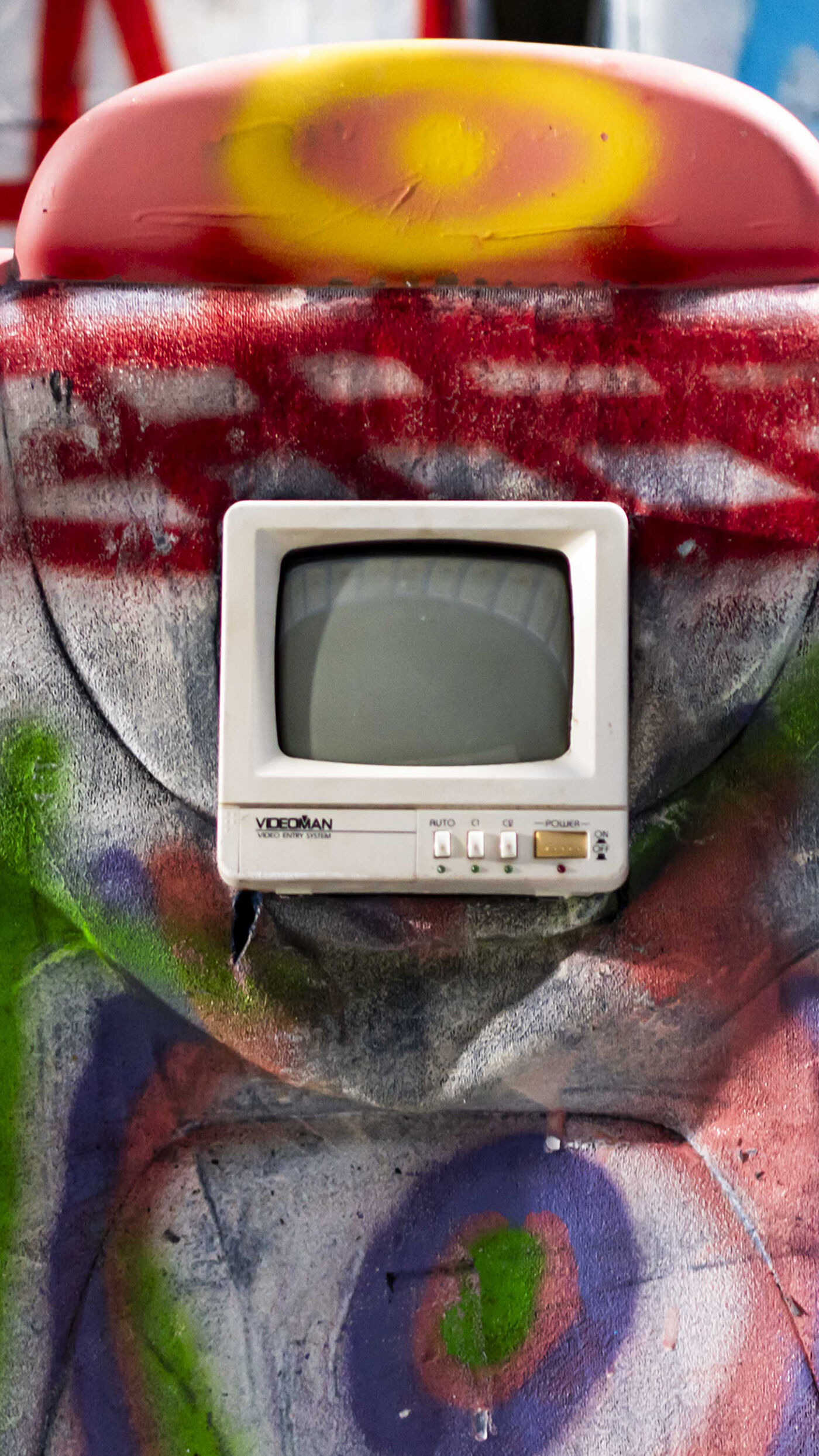 The image showcases a small, vintage television set mounted on a surface covered in colorful graffiti. The TV is white with a square screen.