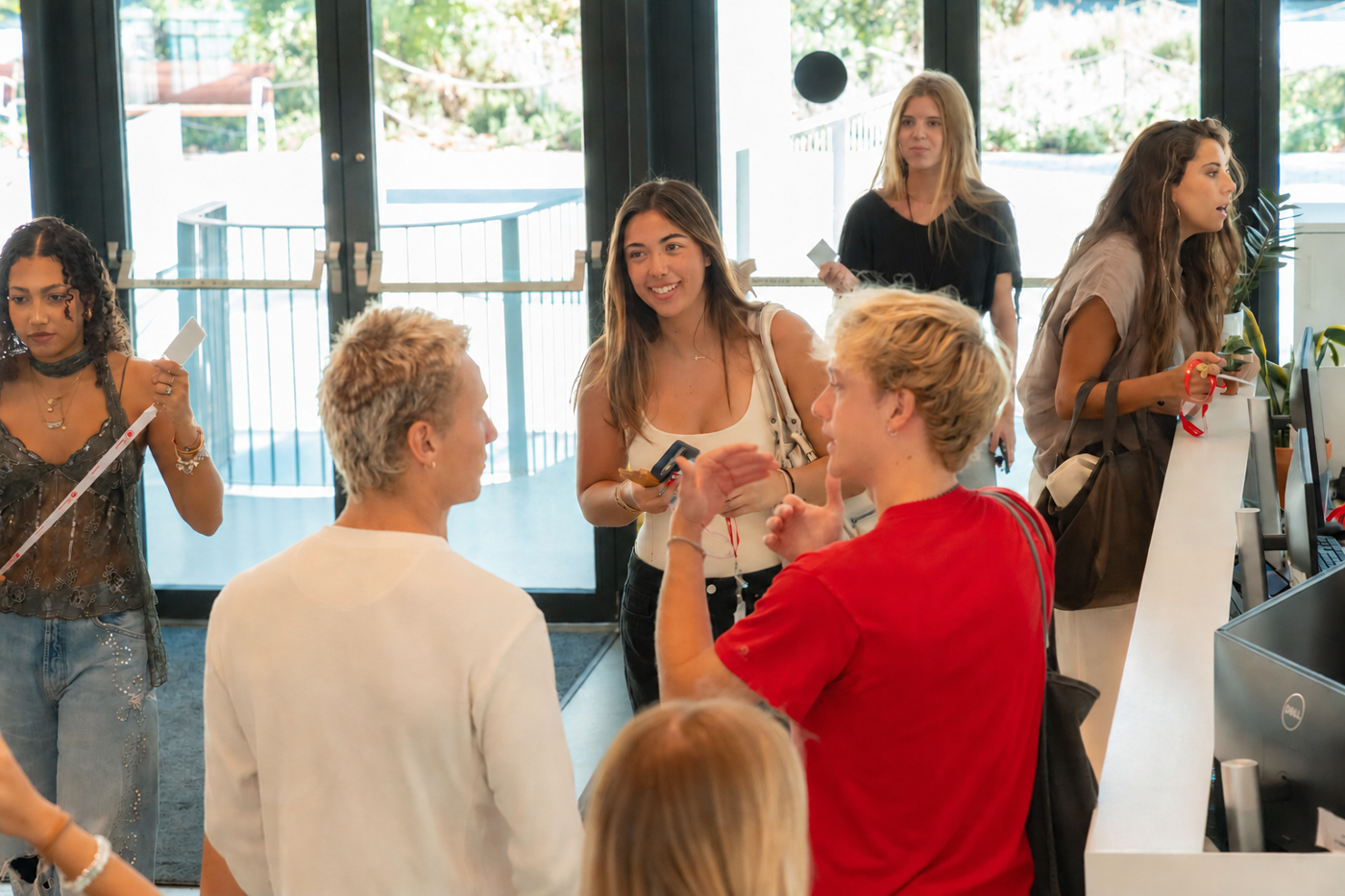 A group of young people are gathered indoors, appearing to be interacting and talking amongst themselves in a casual setting.