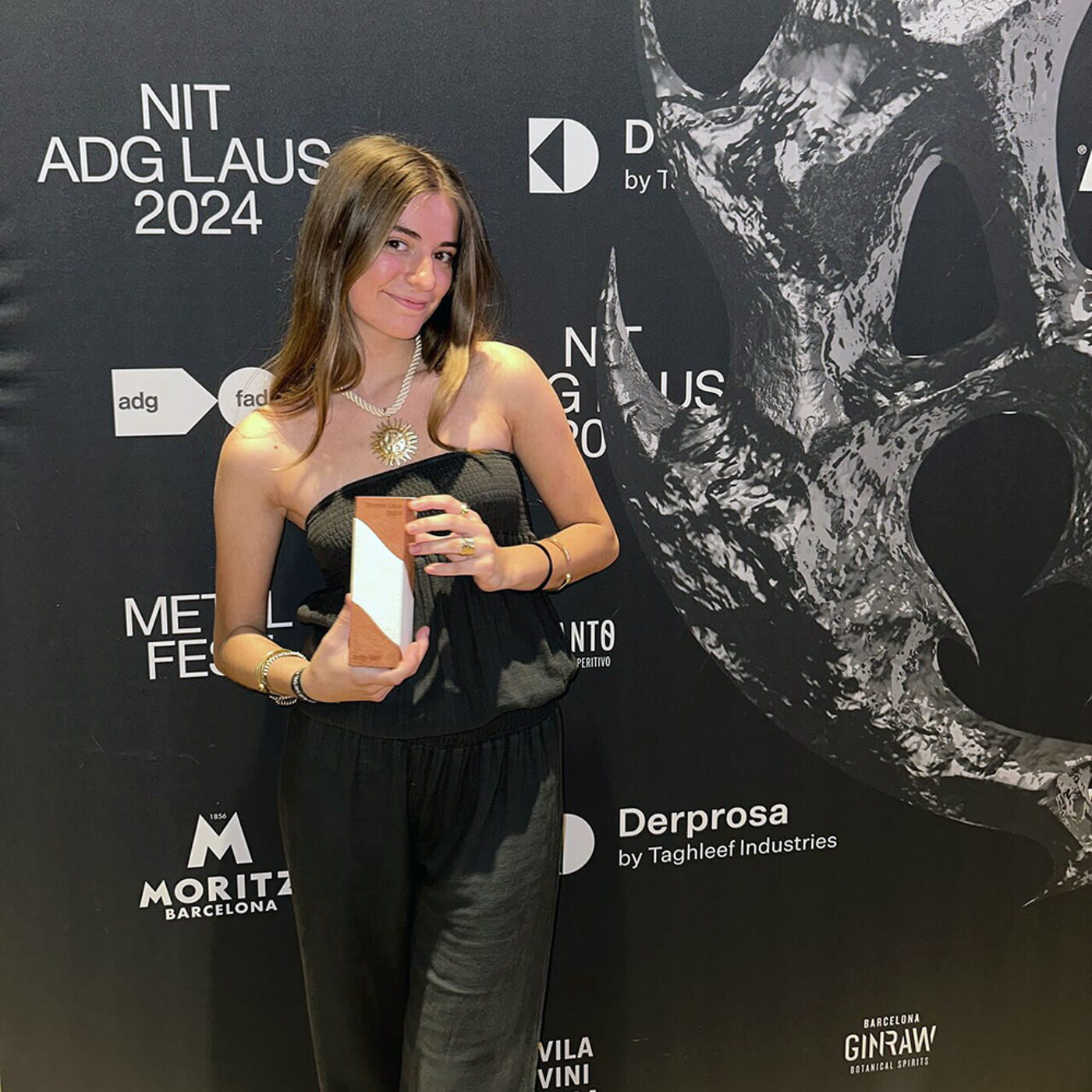 A woman poses with her award at the Nit ADG Laus 2024 event. The black backdrop features logos and artistic designs, highlighting the prestigious ceremony celebrating design and creativity in Barcelona.