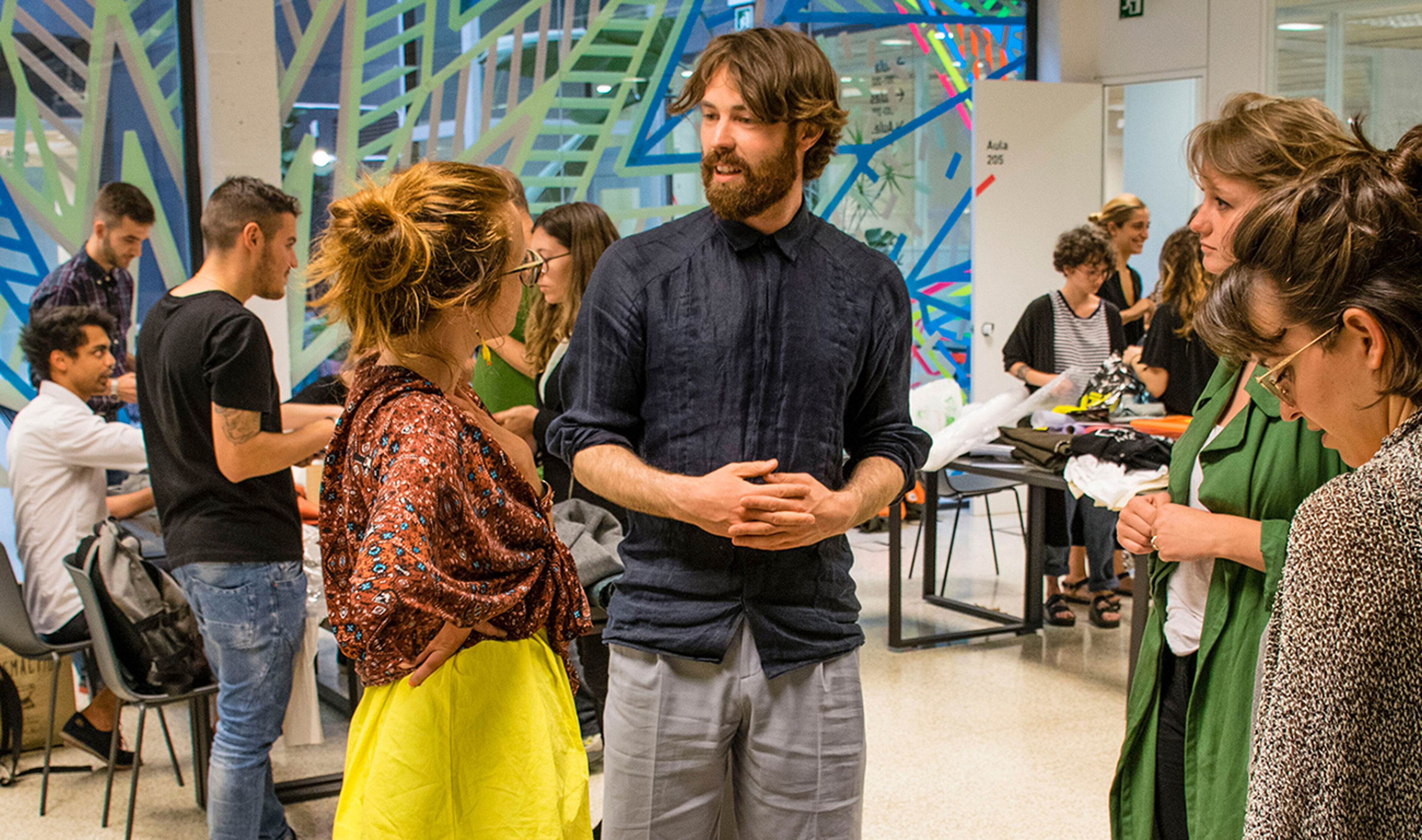 A group of individuals engaged in conversation at a creative workshop with vibrant artwork in the background.
