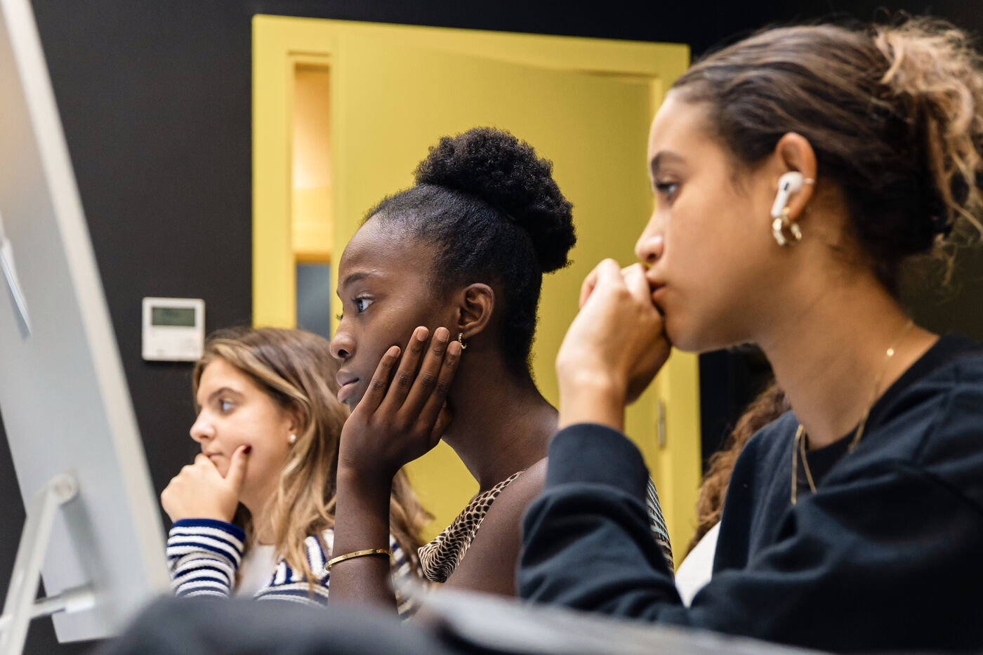 Three students deeply focused and listening intently during a learning session, with a computer monitor in the foreground.