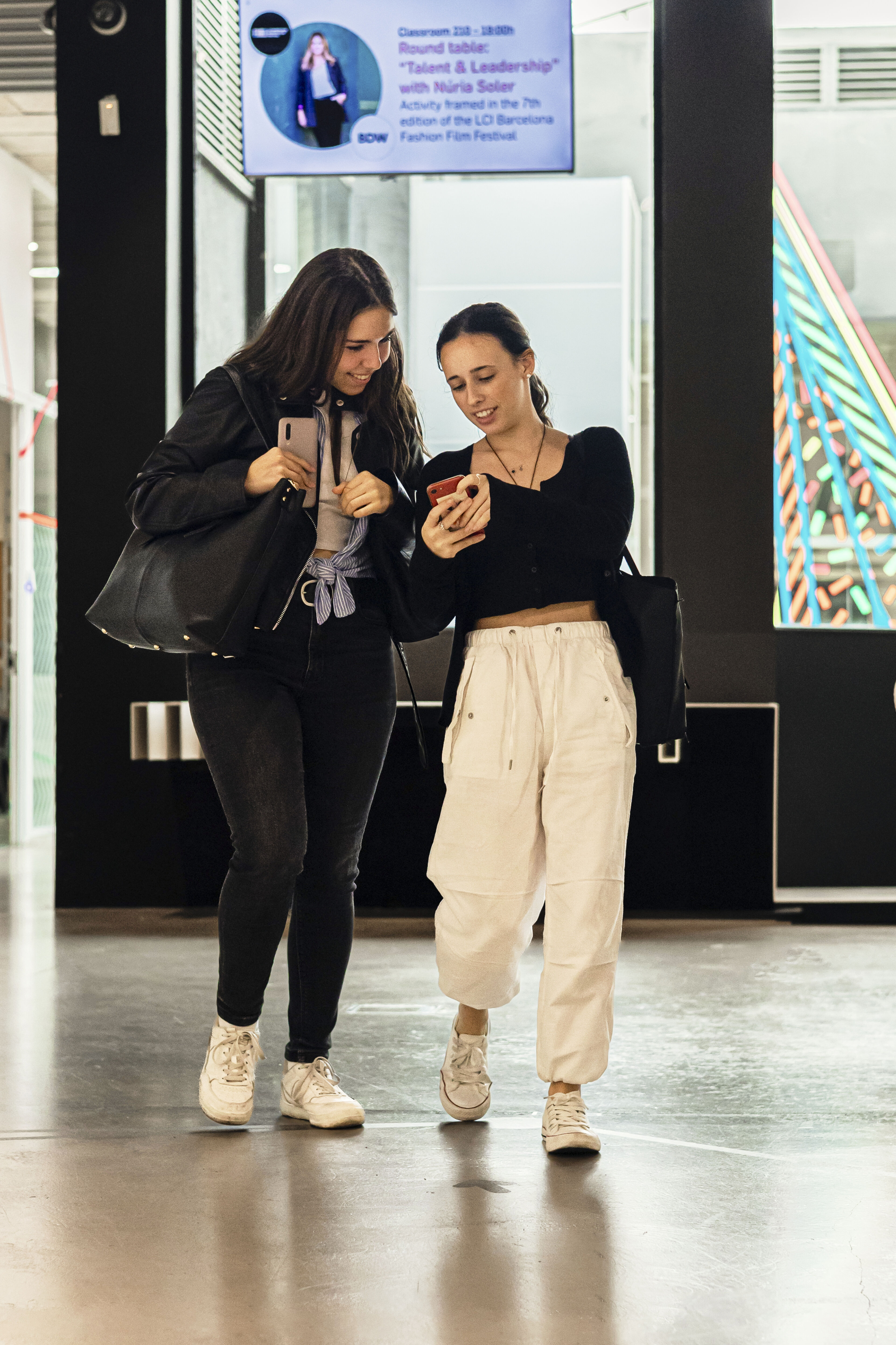 Two women walking and looking at a smartphone together, sharing a moment.