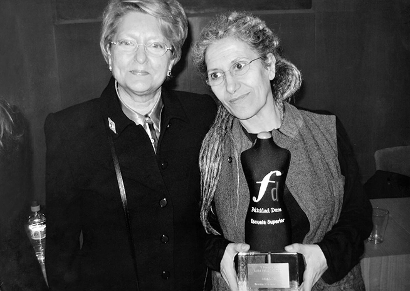 Two women posing with an award, one holding a plaque, in a black and white photograph.