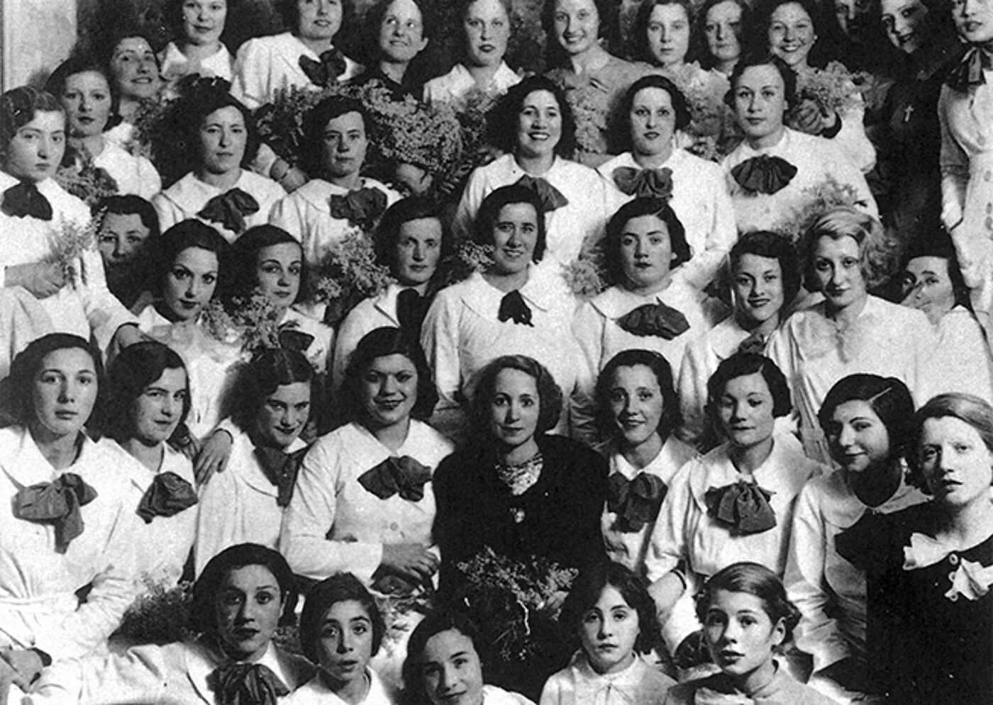 Black and white historical photograph of a large group of women in formal attire with corsages.