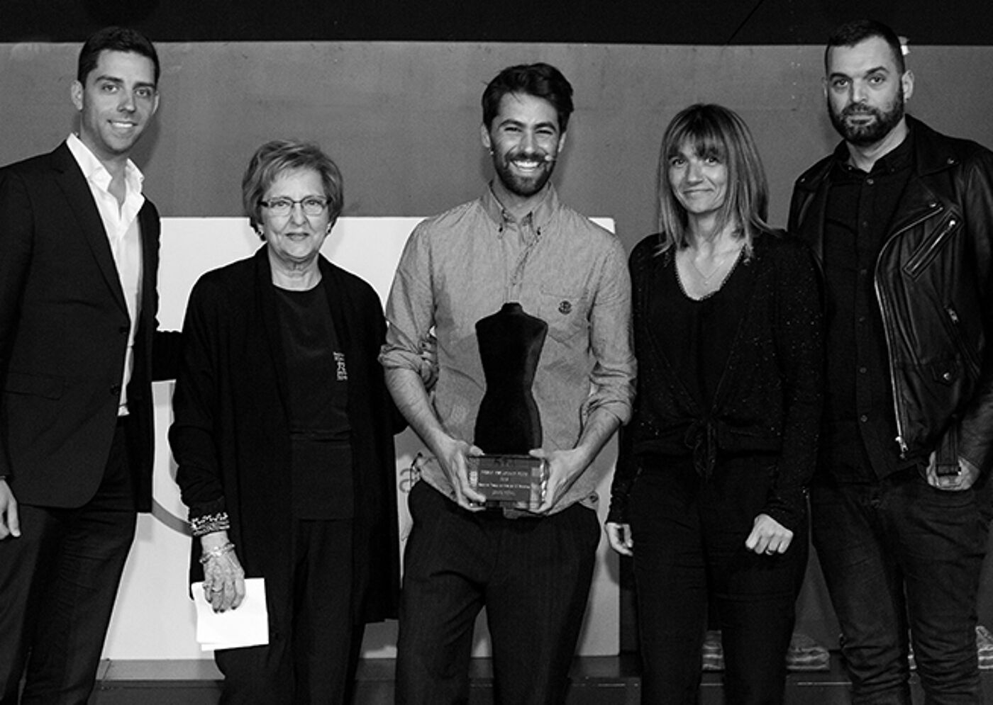 Five individuals smiling at an award ceremony, with the central person holding a trophy.