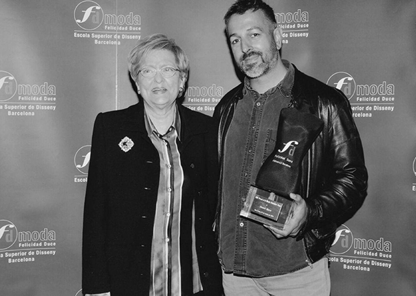 A woman and a man posing at a design school event, with the man holding an award.
