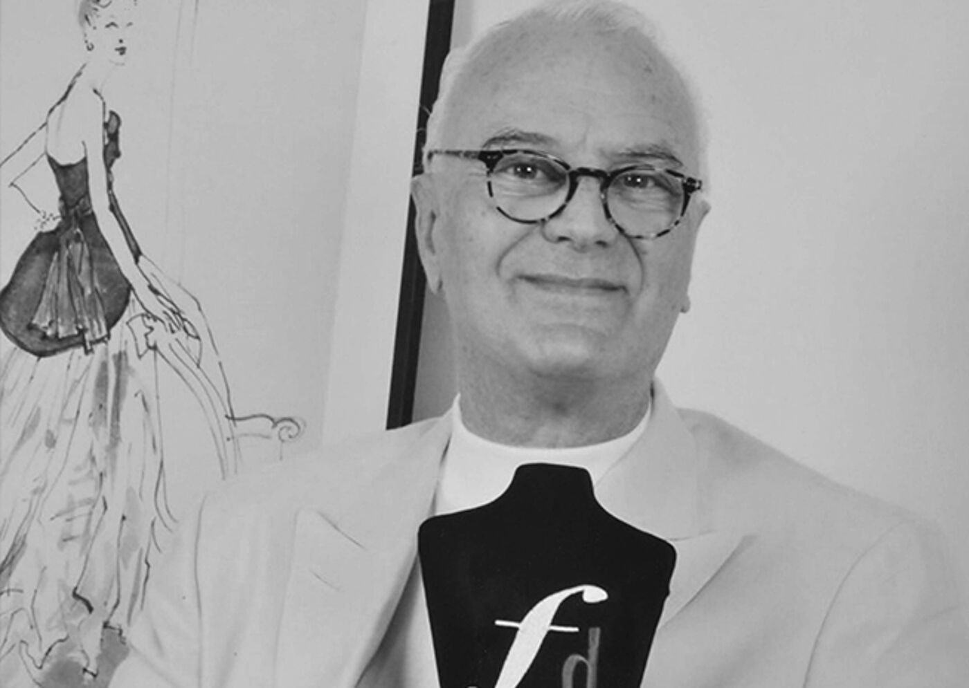 A monochrome photo of a fashion designer holding an award with an 'f' emblem, with a sketch in the background.