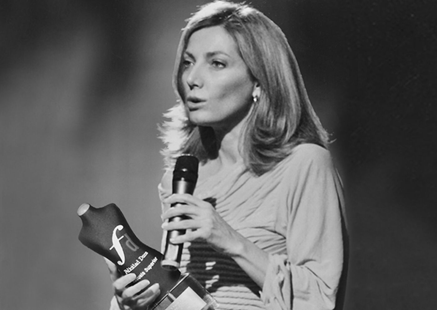 A woman delivers a speech while holding an award, captured in a black and white photograph.