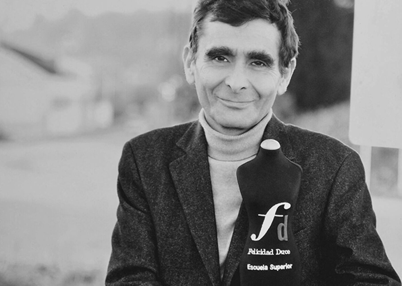 A monochrome portrait of a man smiling while holding an award.