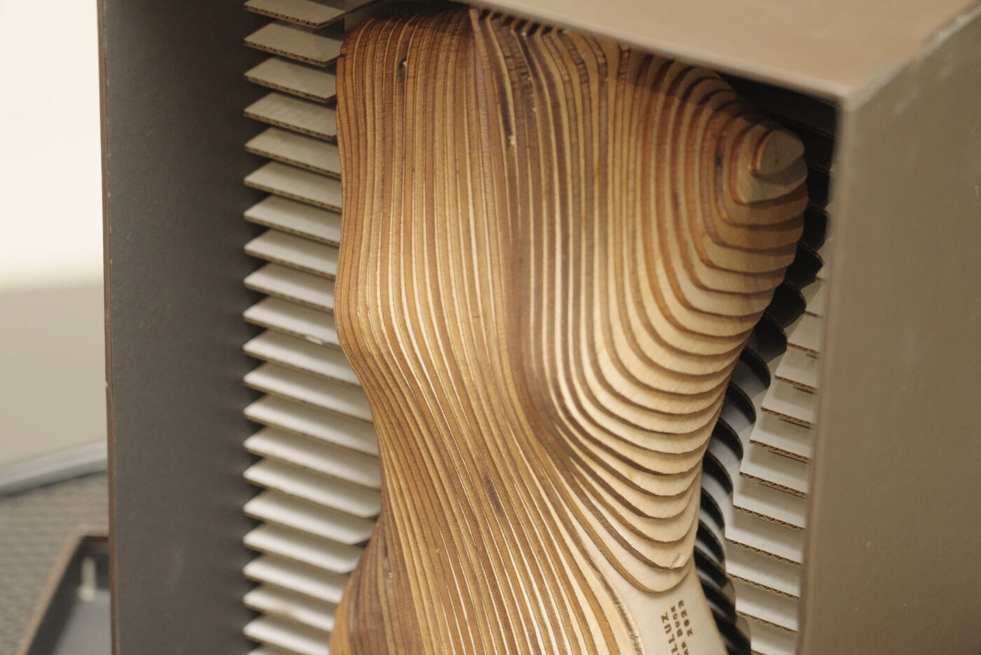 In the image, there is a wooden sculpture of a woman's head or a wooden doll head, which is placed on top of a metal grate or a metal mesh. The sculpture is positioned on a shelf or a table, and it appears to be a unique and artistic piece.