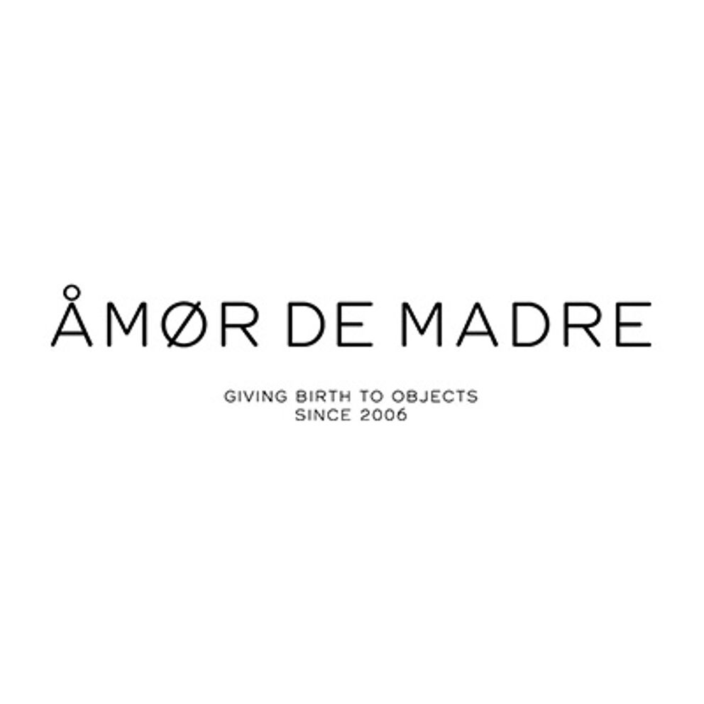 The logo spells "ÁMOR DE MADRE" in a bold serif font with an accented 'Á', accompanied by the slogan "GIVING BIRTH TO OBJECTS SINCE 2006" in a smaller sans-serif font.