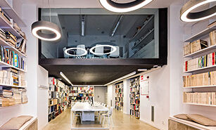 Espacio de biblioteca contemporánea con luminarias circulares, mesa comunal central y estanterías de libros de pared a pared.