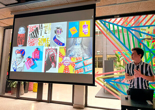 Una persona está presentando junto a una pantalla que muestra un collage de vibrantes piezas de arte contemporáneo.