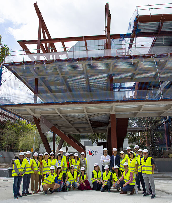 A group of professionals wearing safety gear in front of an under-construction building with scaffolding.