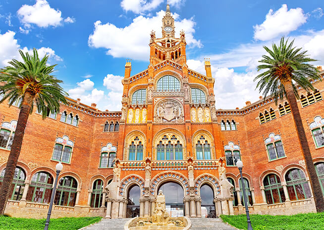 The intricate modernist façade of Hospital de Sant Pau, a UNESCO World Heritage Site in Barcelona, Spain, surrounded by palm trees.