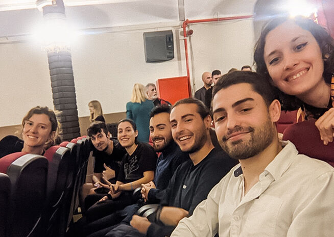 Un grup d'amics joves somrient i fent-se un selfie en un auditori teatral.