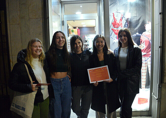 Un grupo de mujeres alegres está fuera de una tienda por la noche, mostrando con orgullo un certificado de logro.